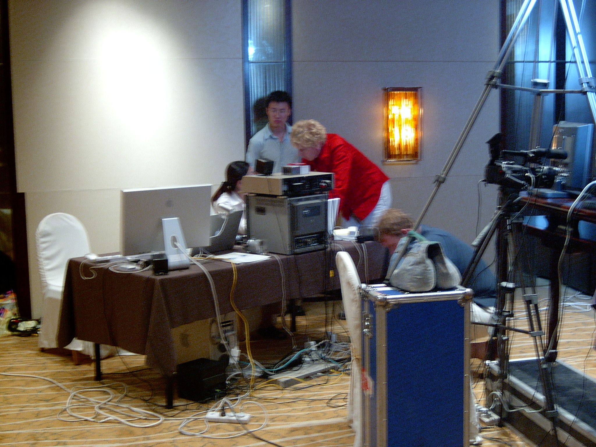 Crew setting up streaming equipment on a draped table in a hotel room, with a flight case and camera on a tripod