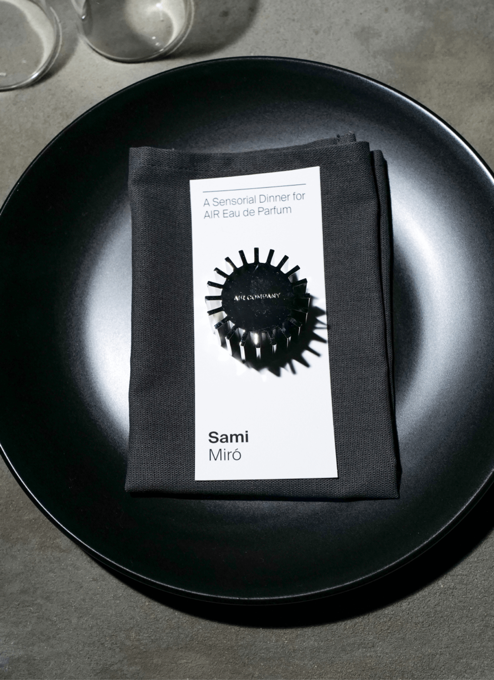 fragrance cap sitting on a table setting with a menu card and a black plate
