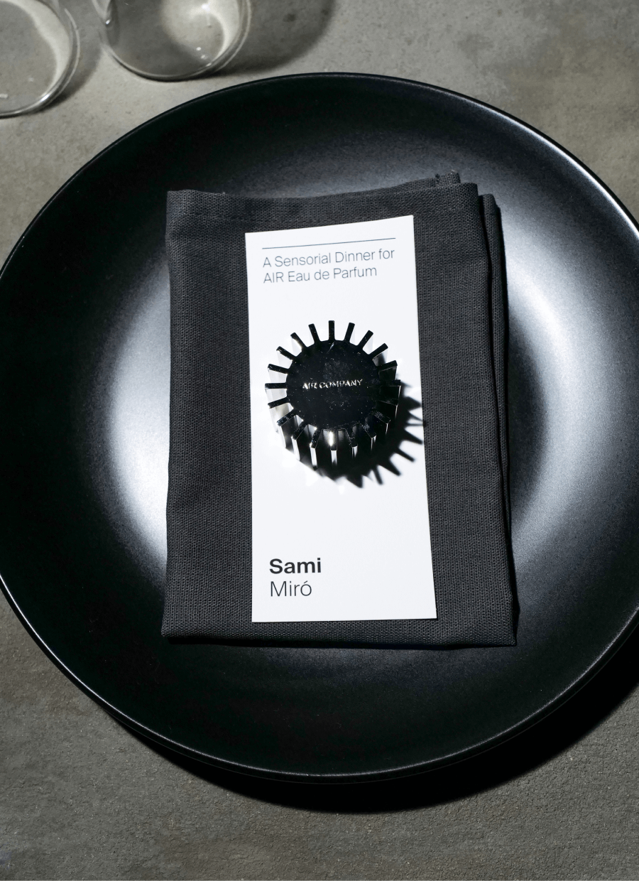 fragrance cap sitting on a table setting with a menu card and a black plate