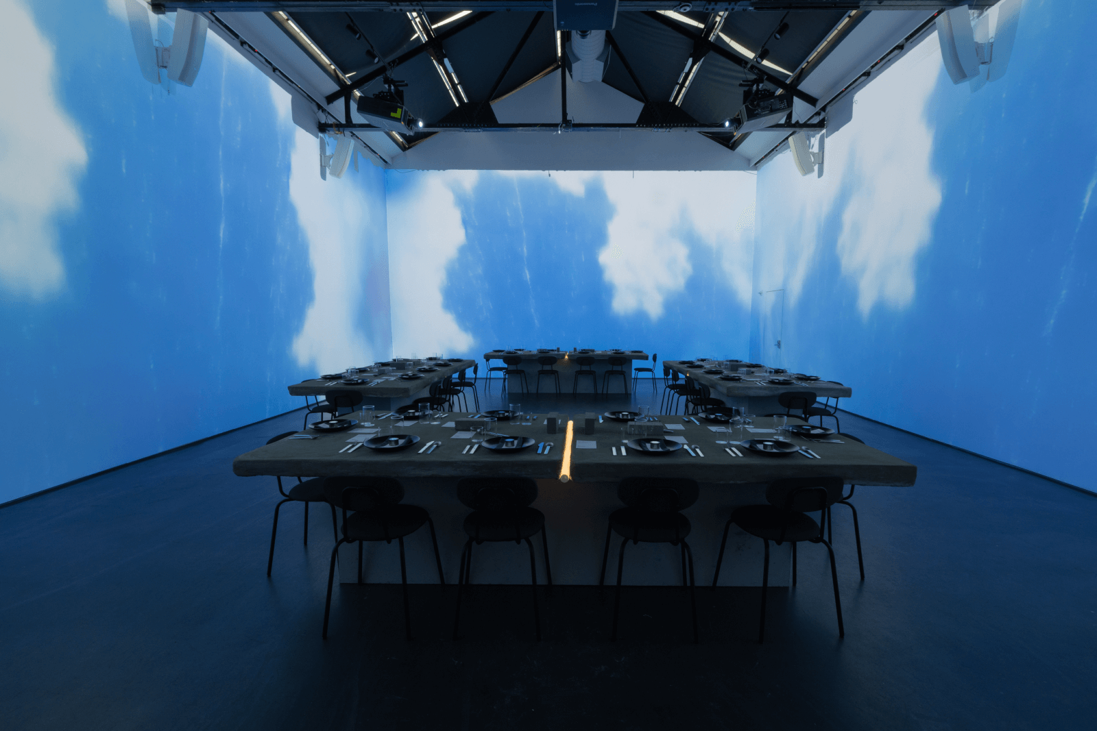 four dinner tables in a room surrounded by projectors showing clouds 