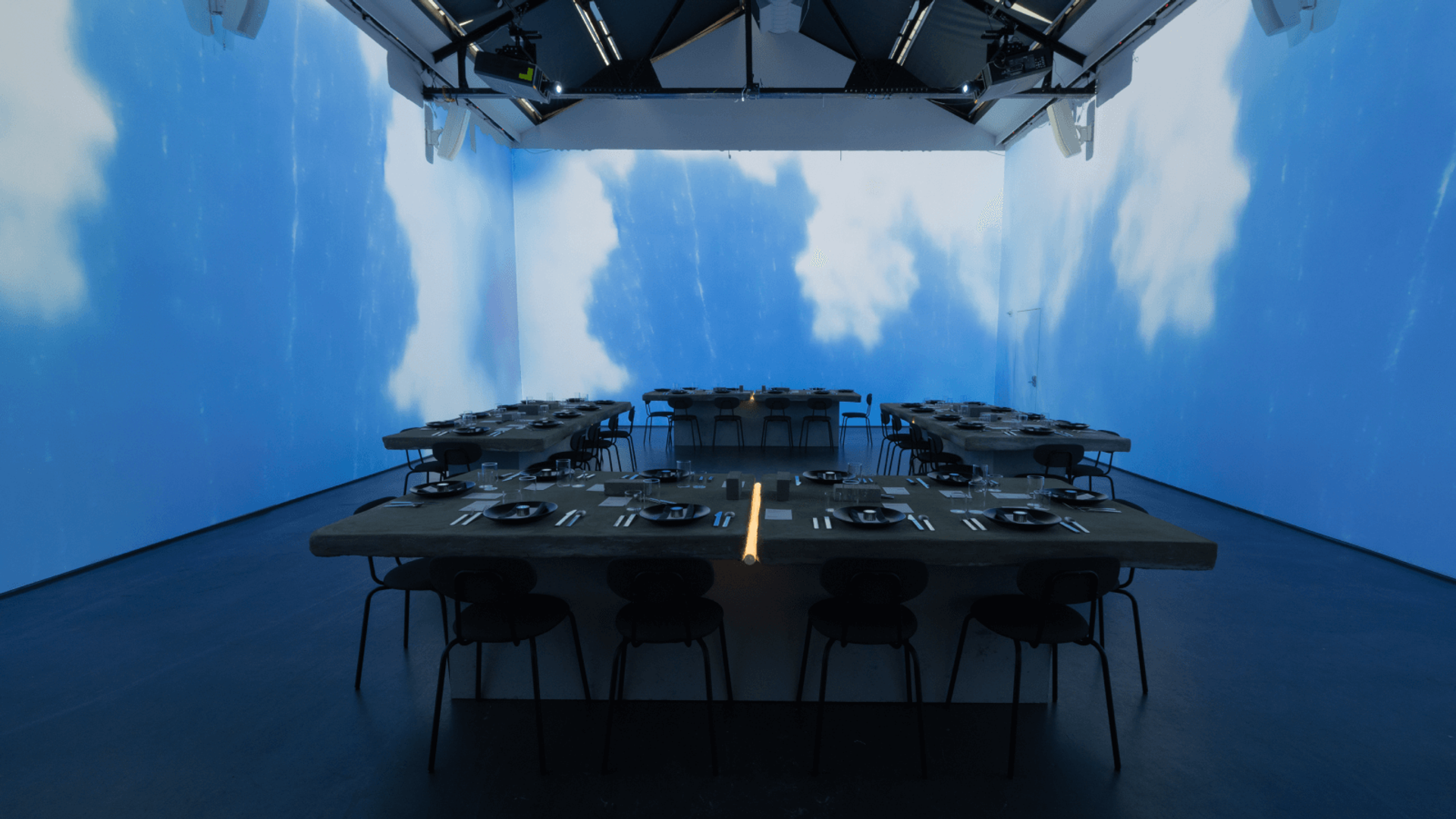 four dinner tables in a room surrounded by projectors showing clouds