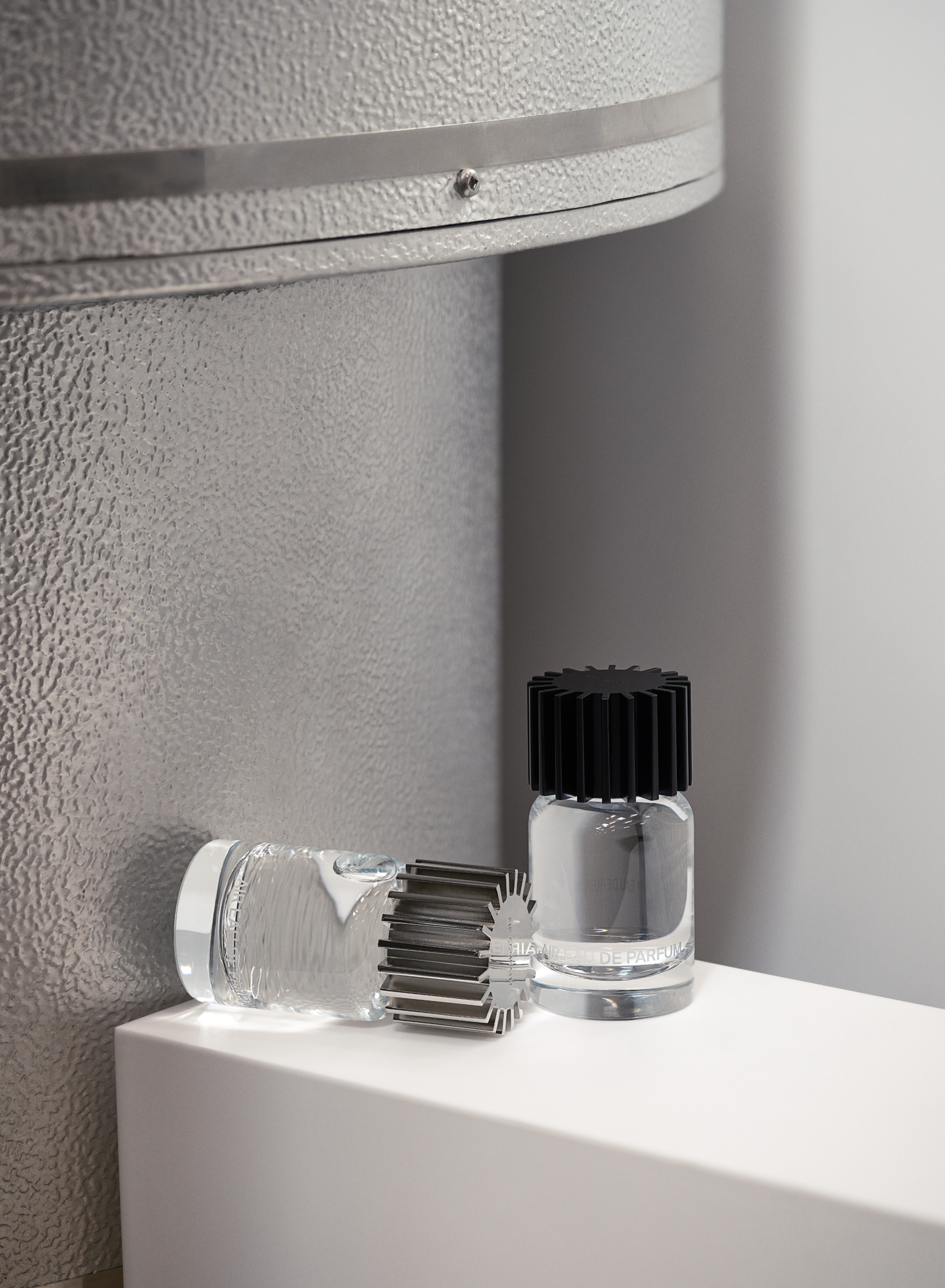 two fragrance bottles up against a metal reactor. one laying down and one standing up.