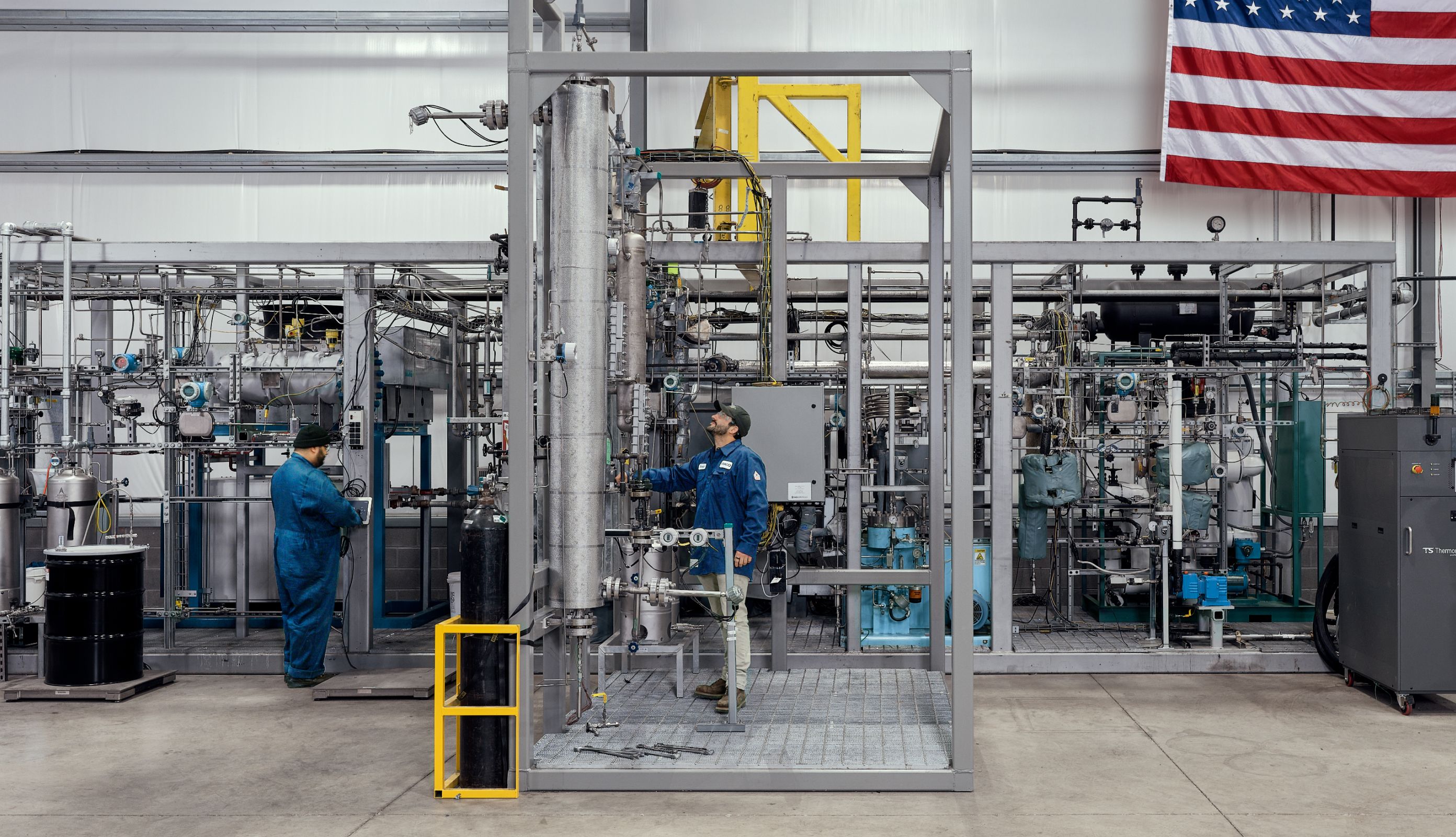 two men working on technology in a facility with an American flag in the background