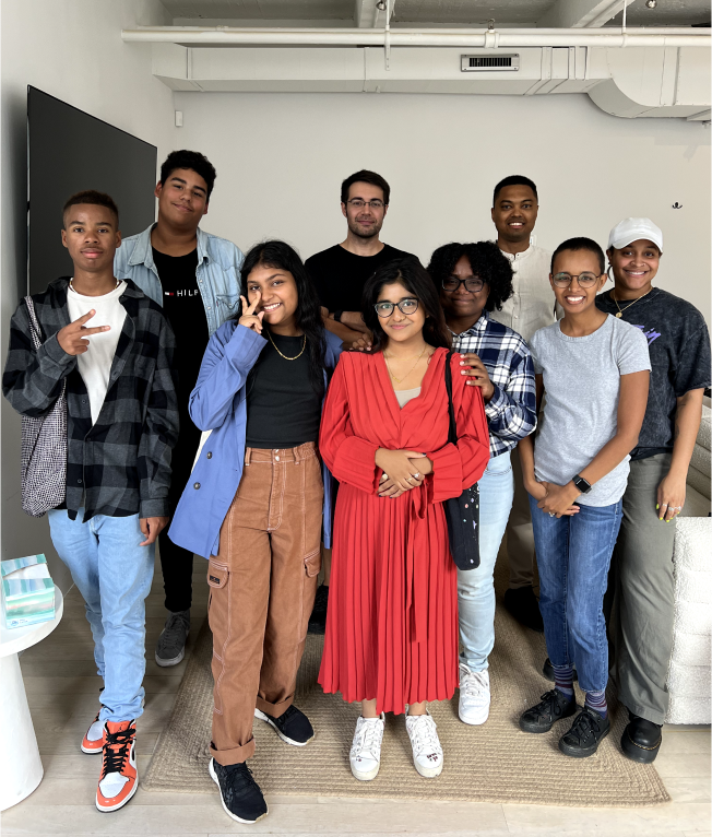 Nine diverse young adults stand together smiling indoors.