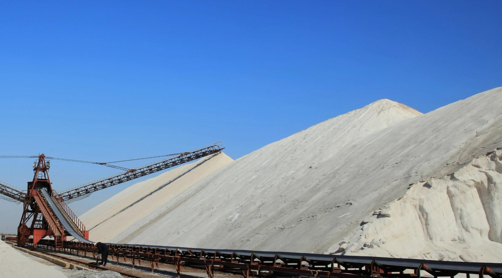 Massive salt piles and industrial conveyors under a bright blue sky.