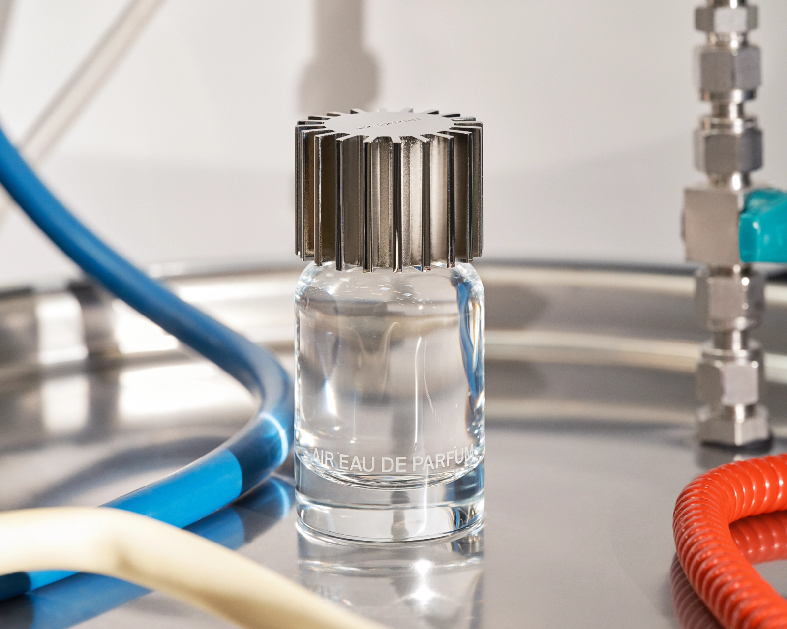 AIR Eau de Parfum fragrance bottle sitting on a silver metal canister with colorful tubes around it.