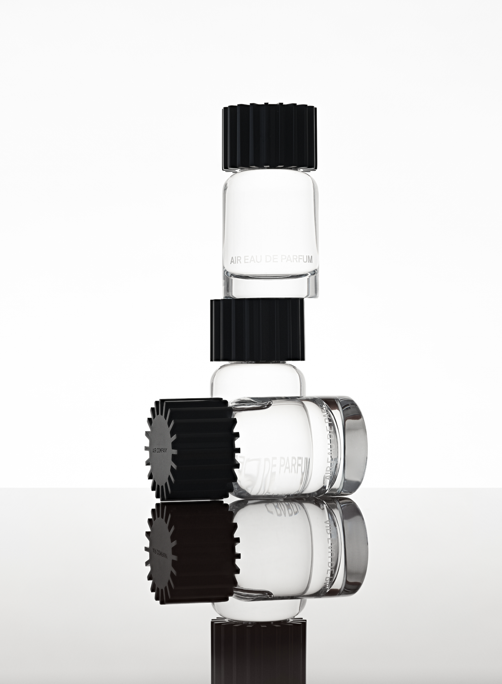 Three glass fragrance bottles, two stacked on top of one another and one laying down in the front on a reflective surface.