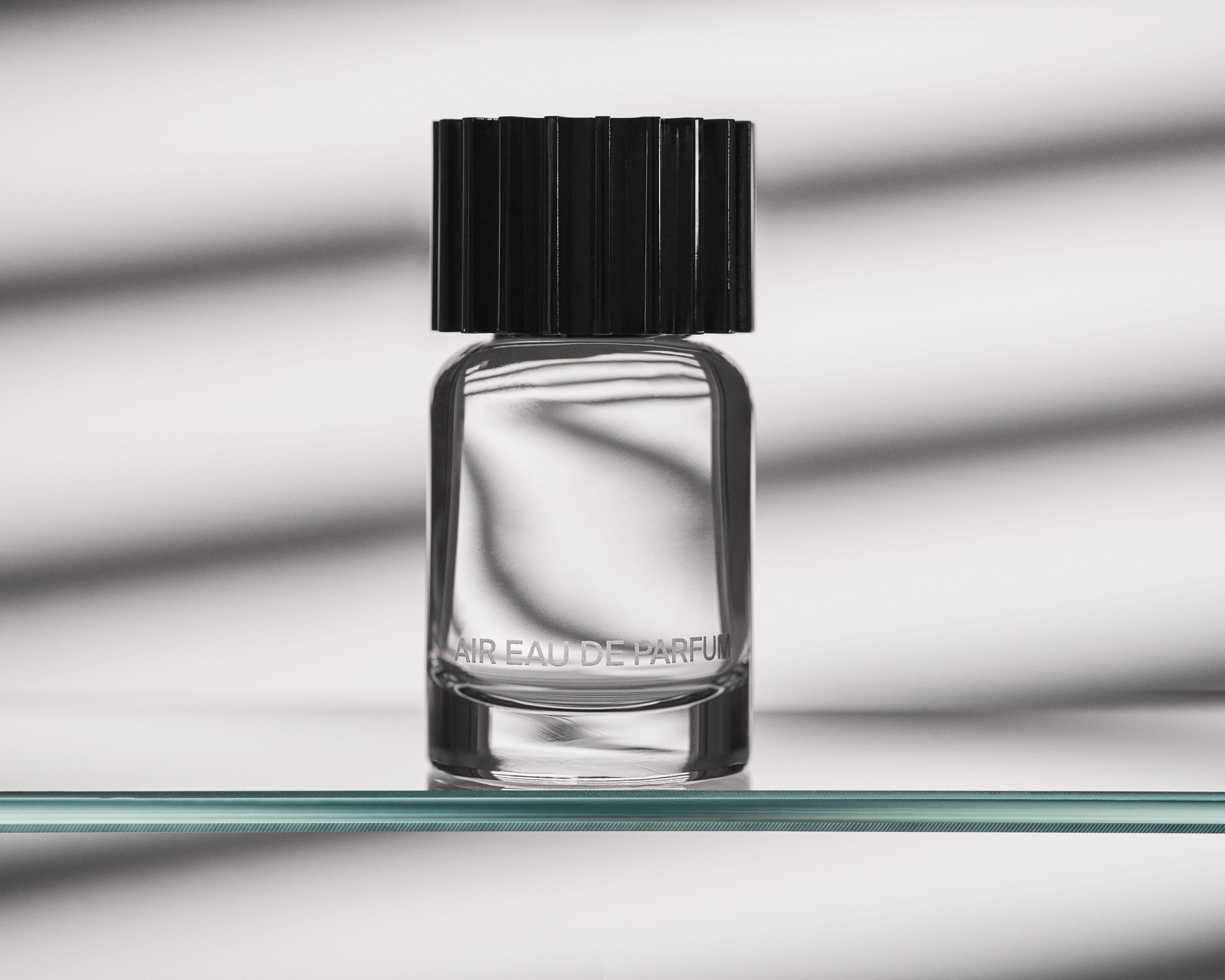 Fragrance bottle, AIR Eau de Parfum, sitting on a clear, glass shelf with shadows behind it. 