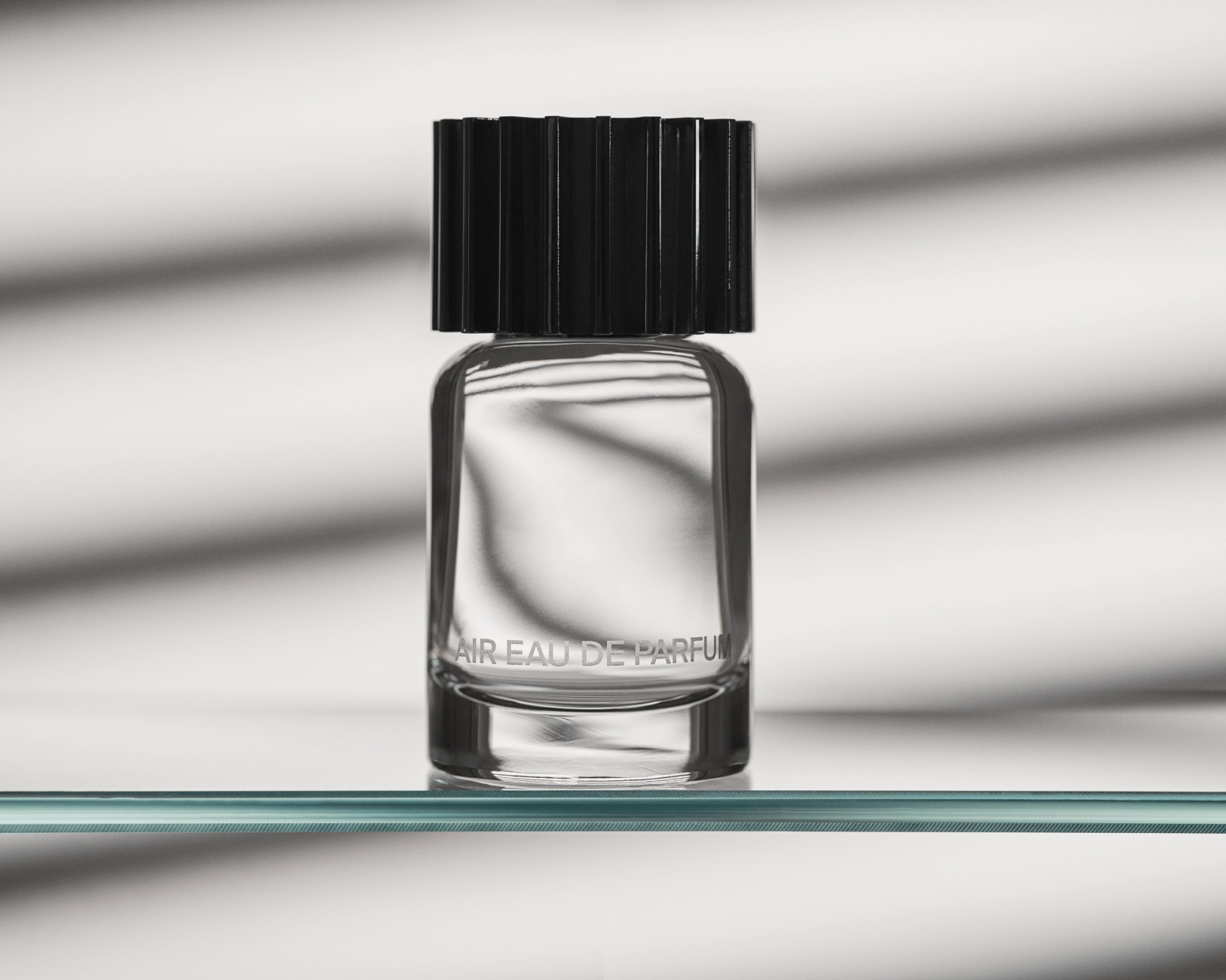 Fragrance bottle, AIR Eau de Parfum, sitting on a clear, glass shelf with shadows behind it.