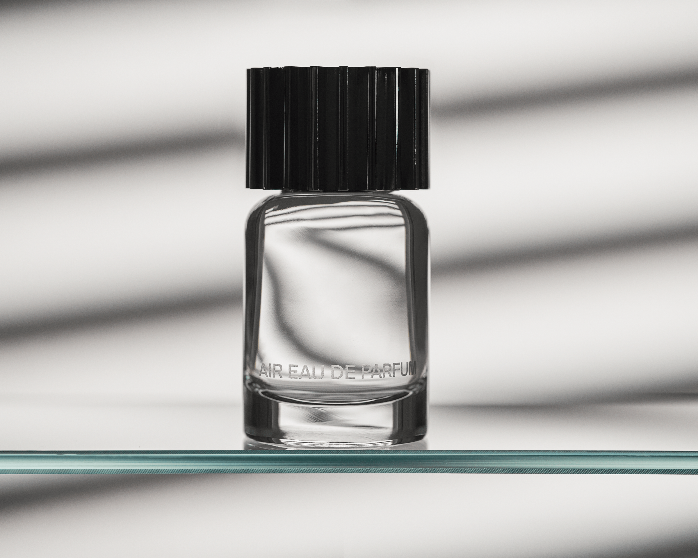 Fragrance bottle, AIR Eau de Parfum, sitting on a clear, glass shelf with shadows behind it.