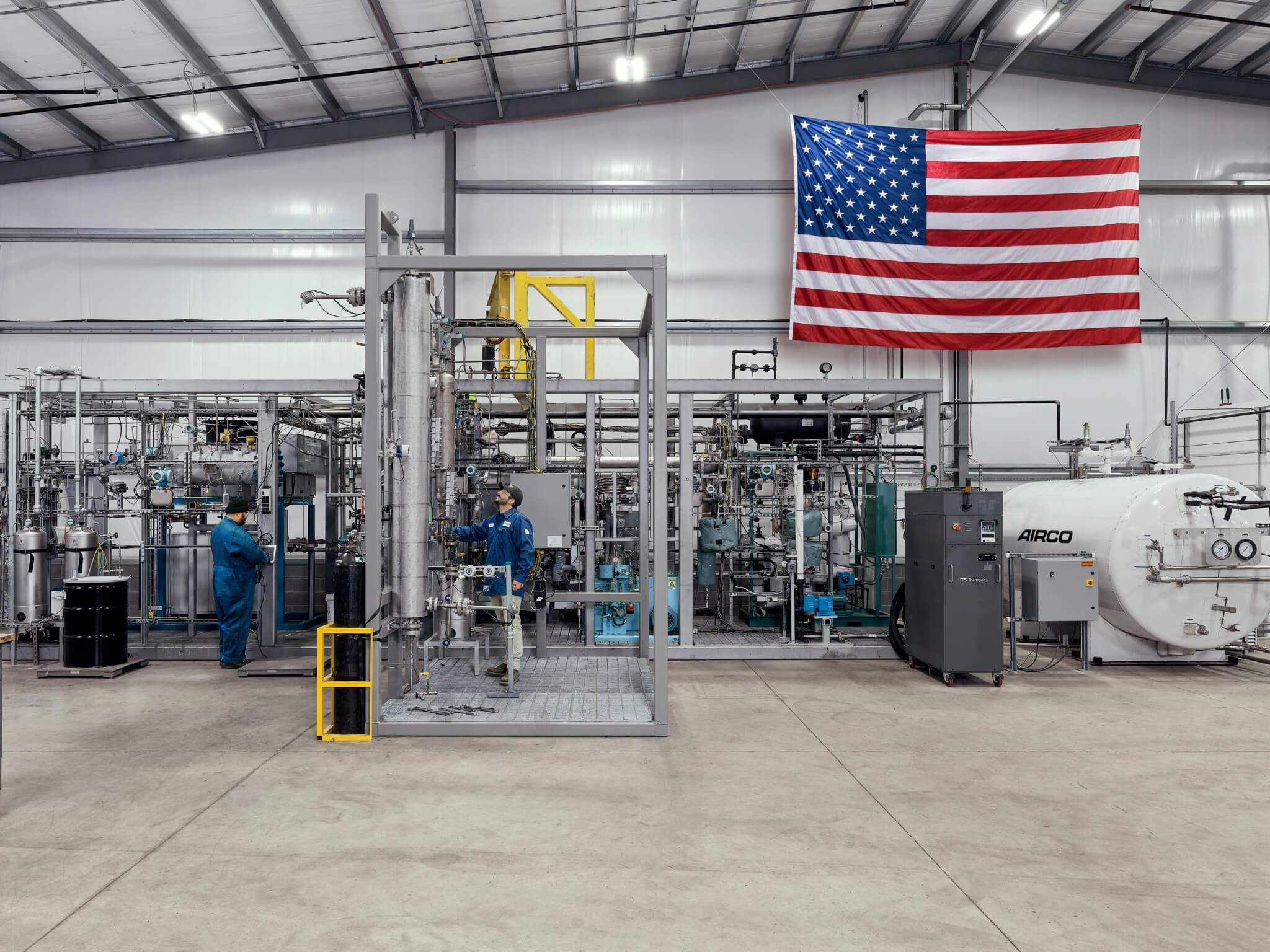 Two men working in an AIRCO facility with the United States of America flag behind them