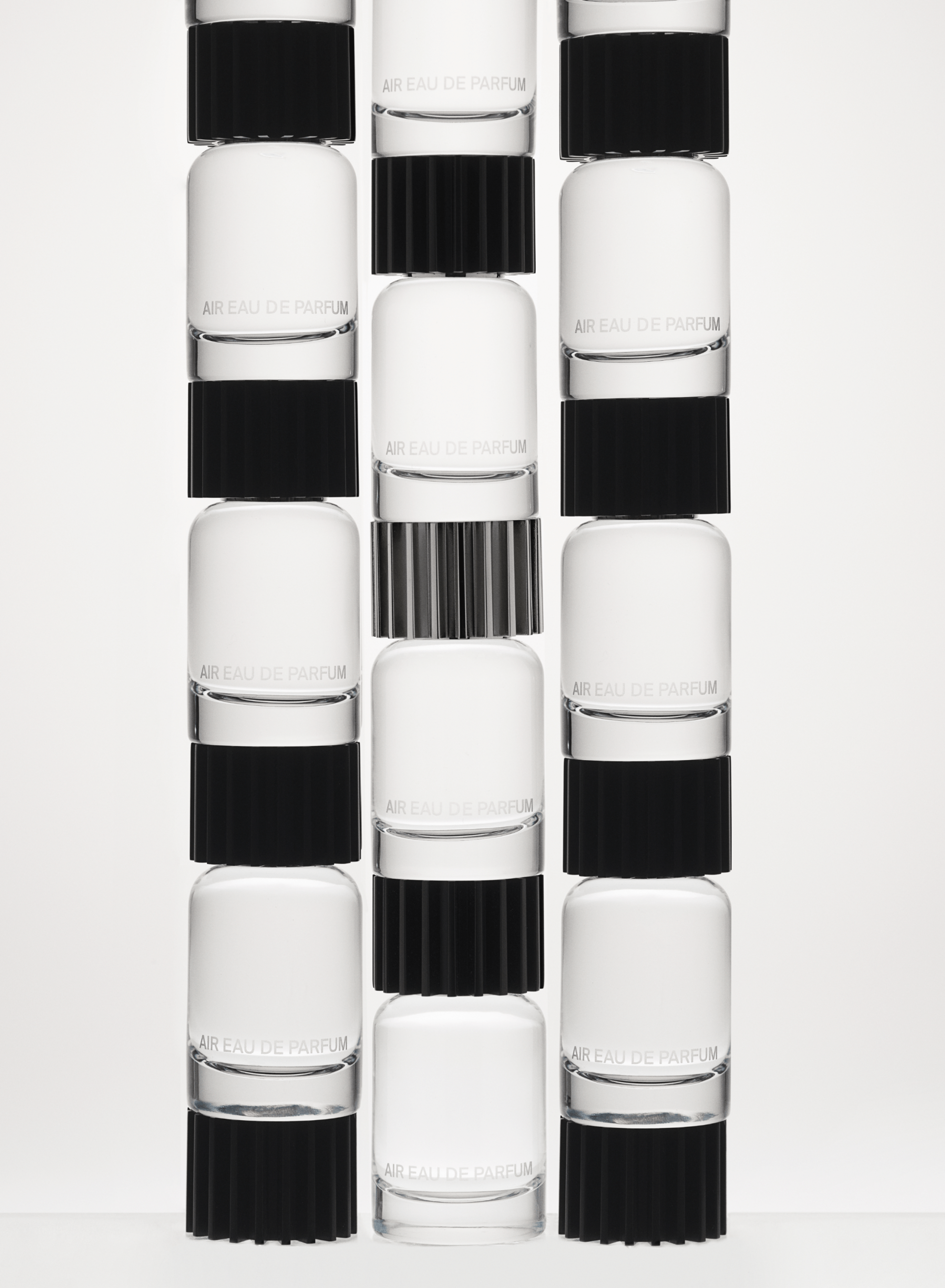 Three columns of glass fragrance bottles stacked on top of one another against a white backdrop