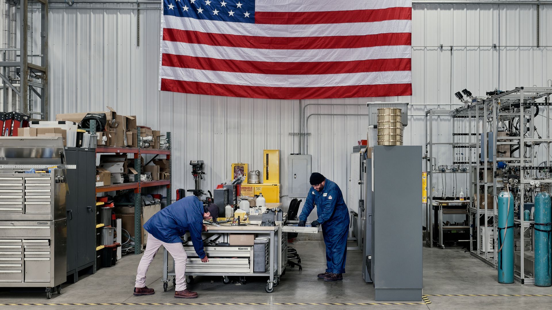 Two AIRCO engineers at work in Pennsylvania manufacturing facility beneath an American flag