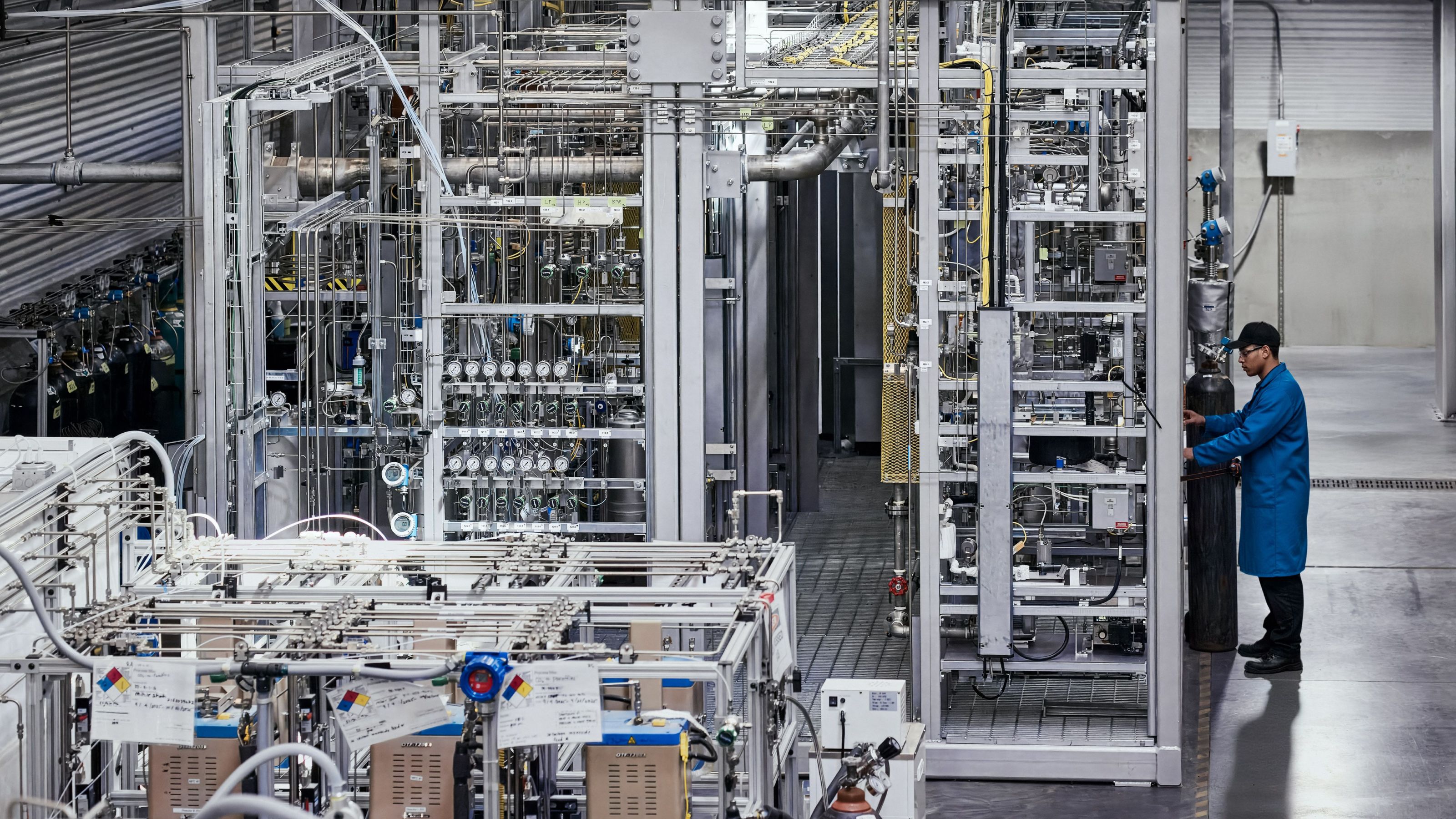 A person in a blue lab coat stands by the AIRCO Fuel Plant