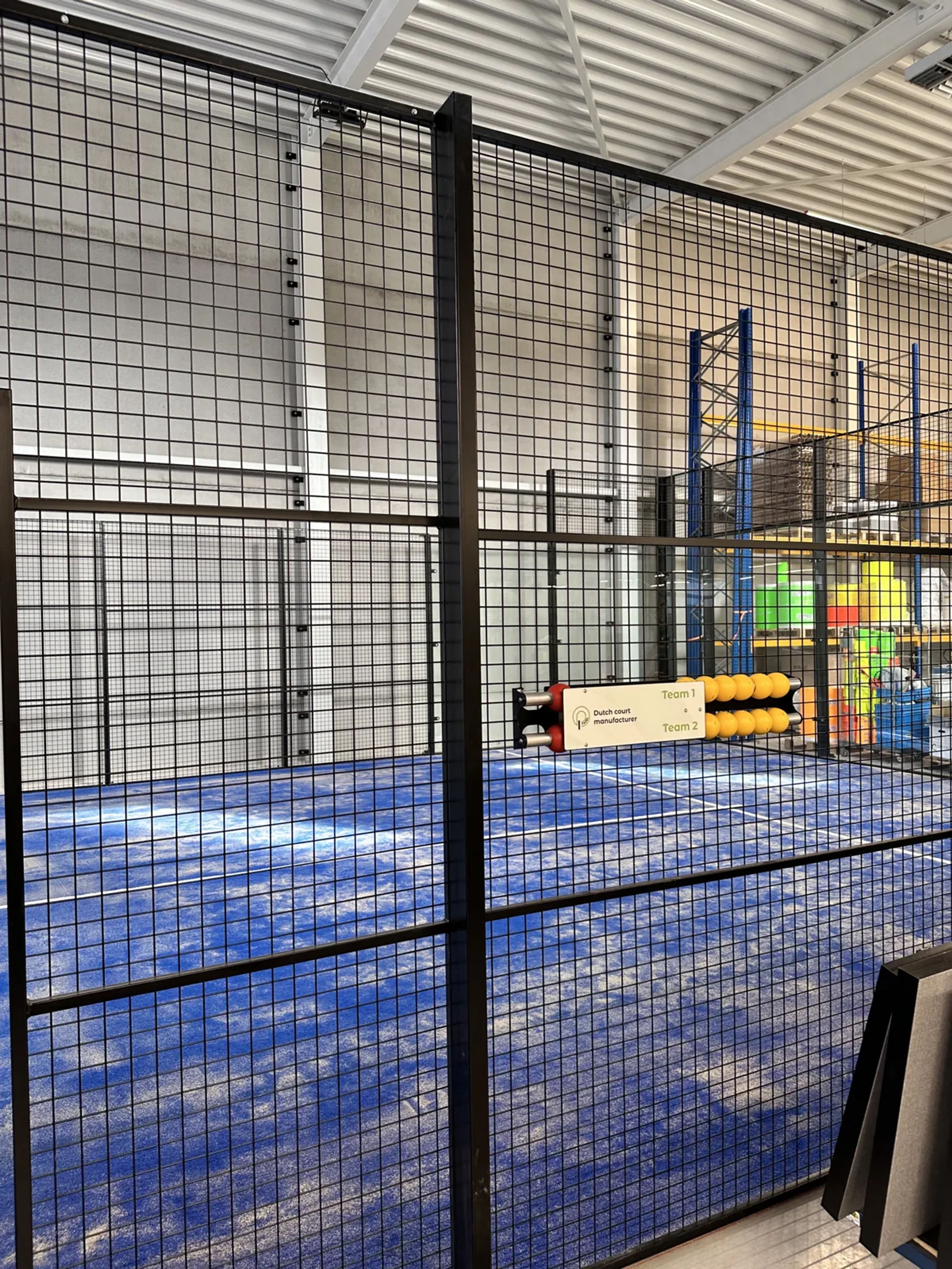 Detail van het stalen frame en de gaaspanelen van een indoor padelbaan in Veldhoven