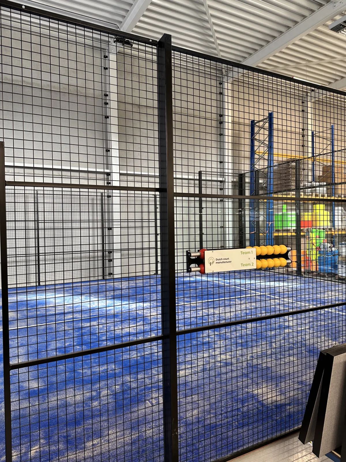 Detail van het stalen frame en de gaaspanelen van een indoor padelbaan in Veldhoven