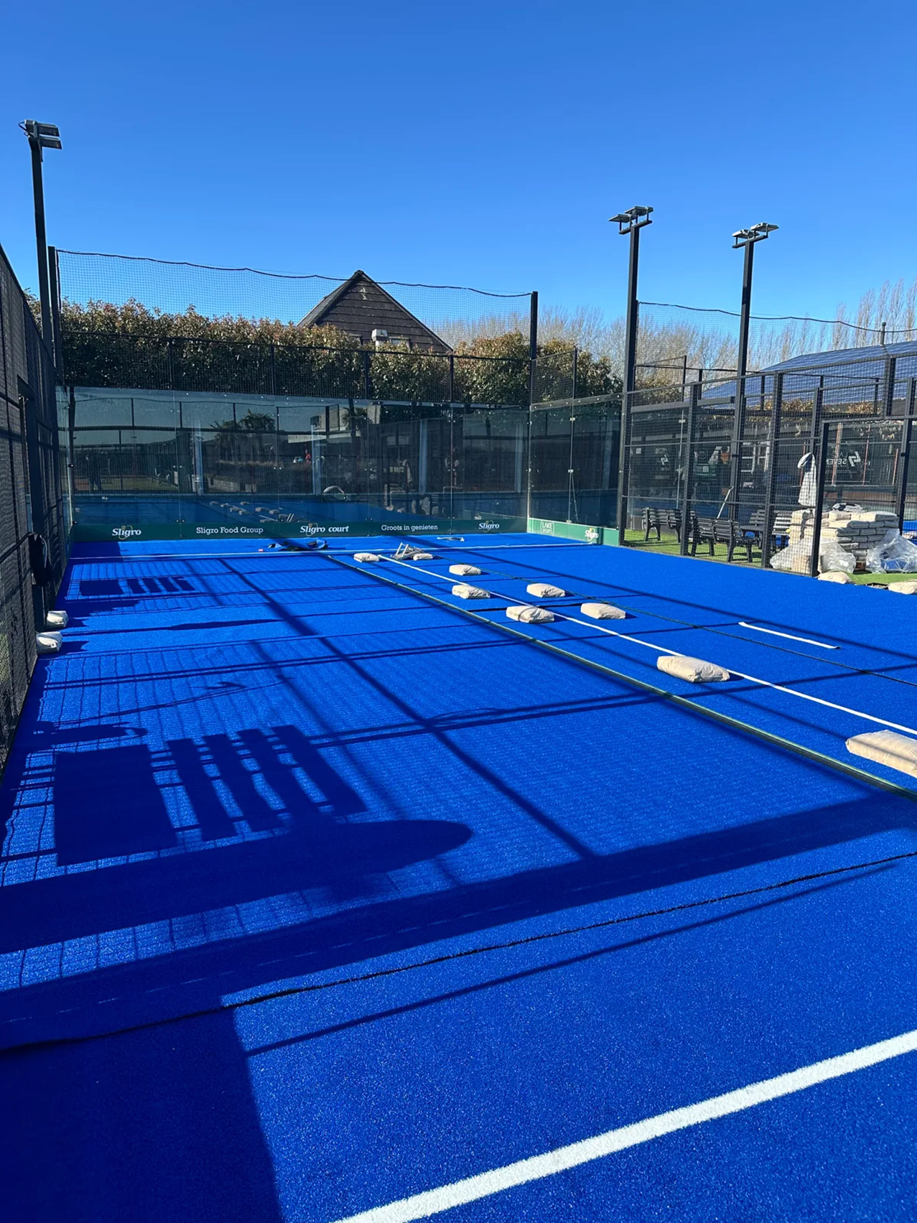 Zandzakken op nieuw blauw kunstgras tijdens het instrooien van een padelbaan