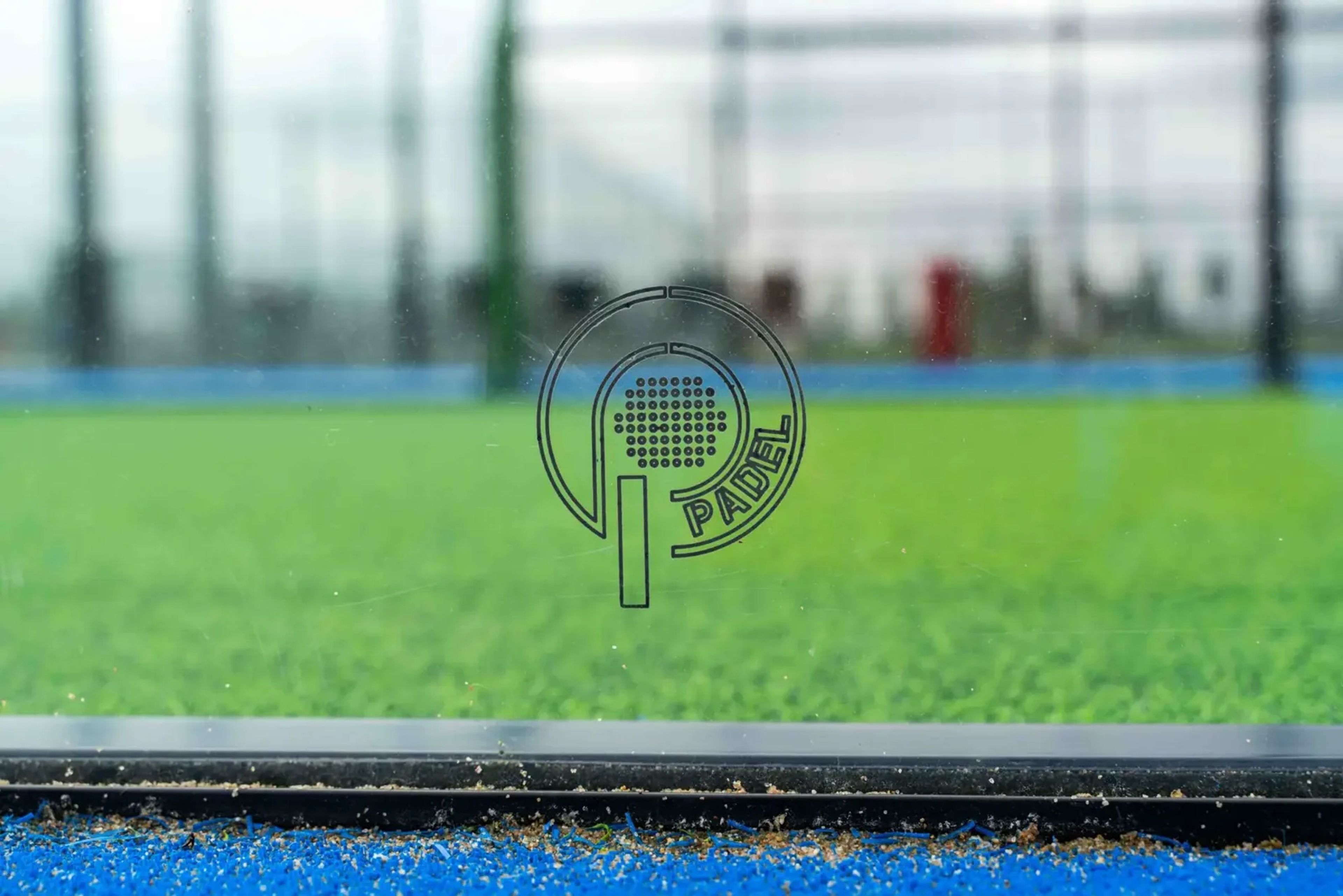 Close-up van het kunstgras met het I-Padel-logo op het glas