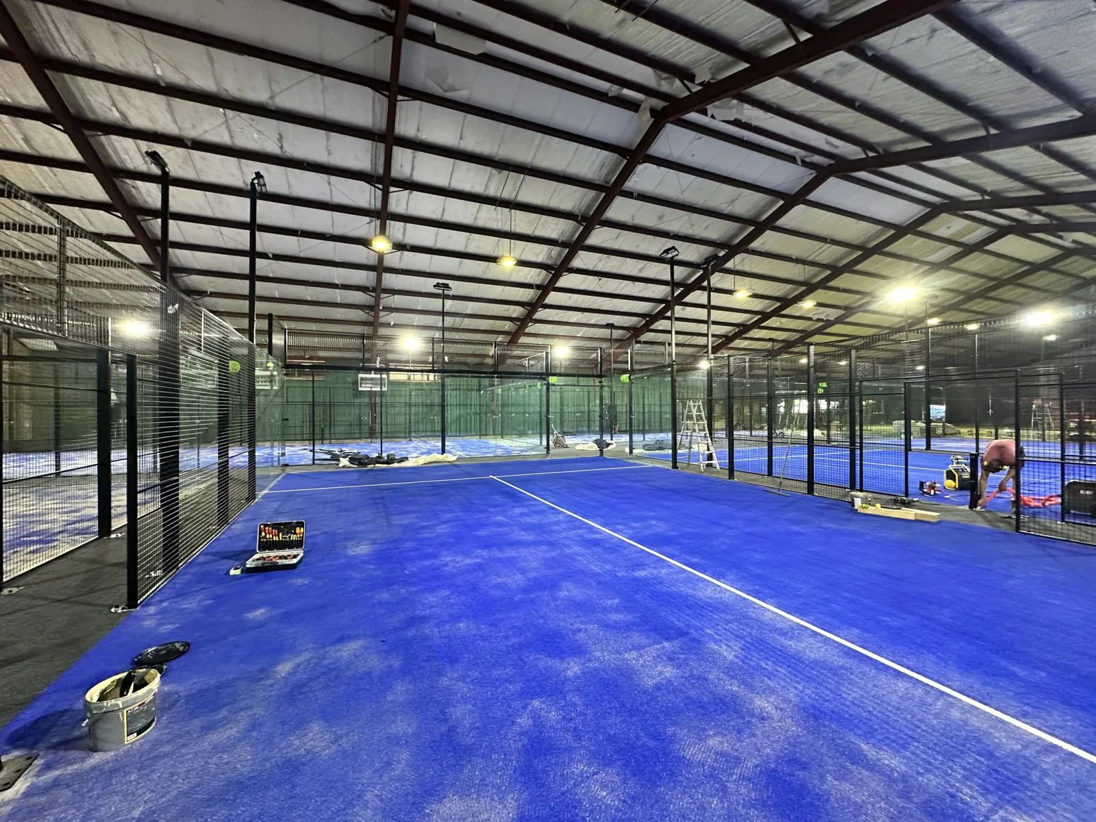 Padelbanen in aanbouw in een stalen hal, met blauw kunstgras