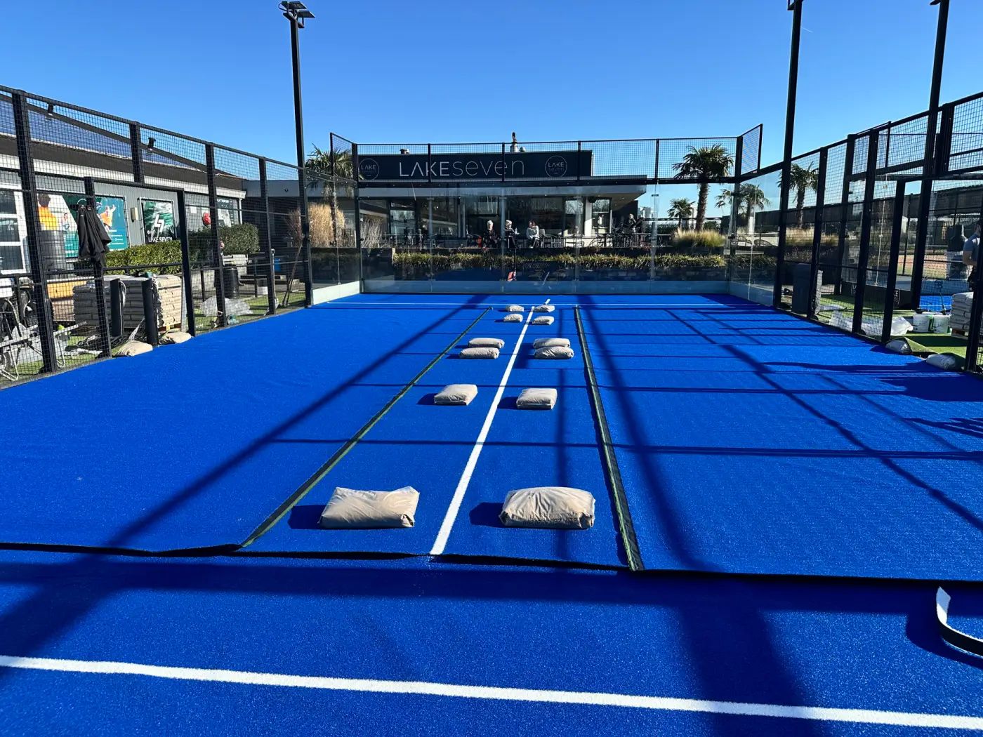 Blauw kunstgras wordt gelegd op een padelbaan, met zandzakken op de naden