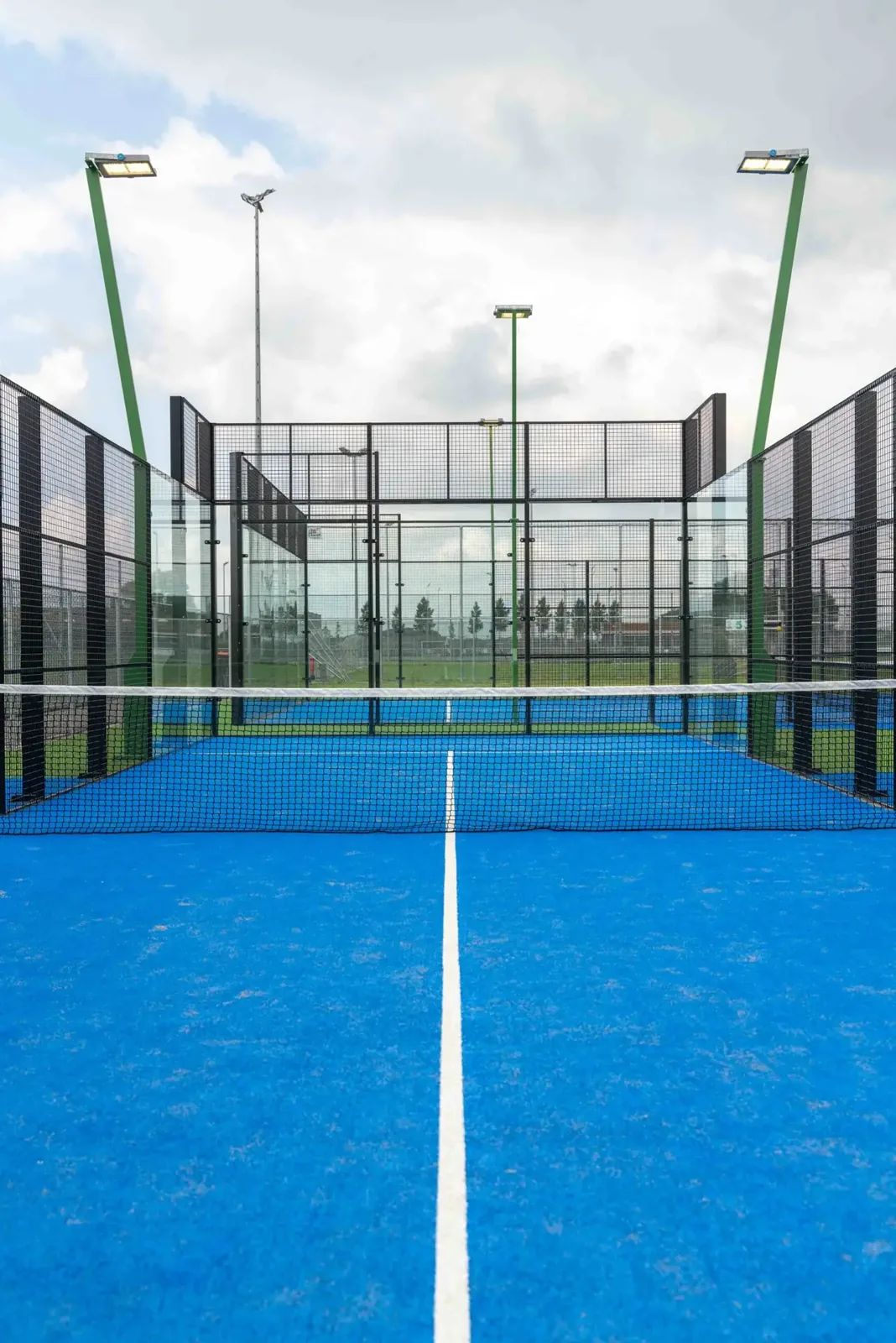 Outdoor padelbaan met blauw kunstgras en groene lichtmastkoppen