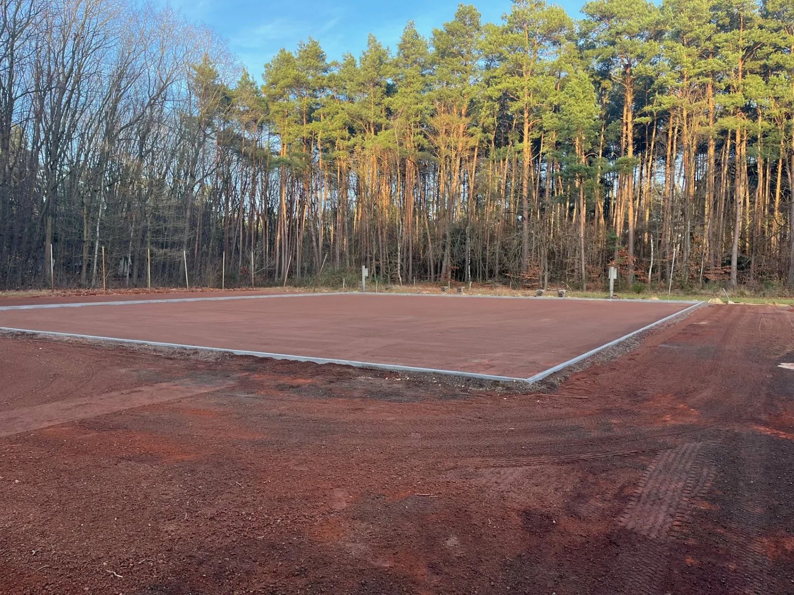 Ringfundering op een rode gravelondergrond in het bos, klaar voor de montage van de padelbanen