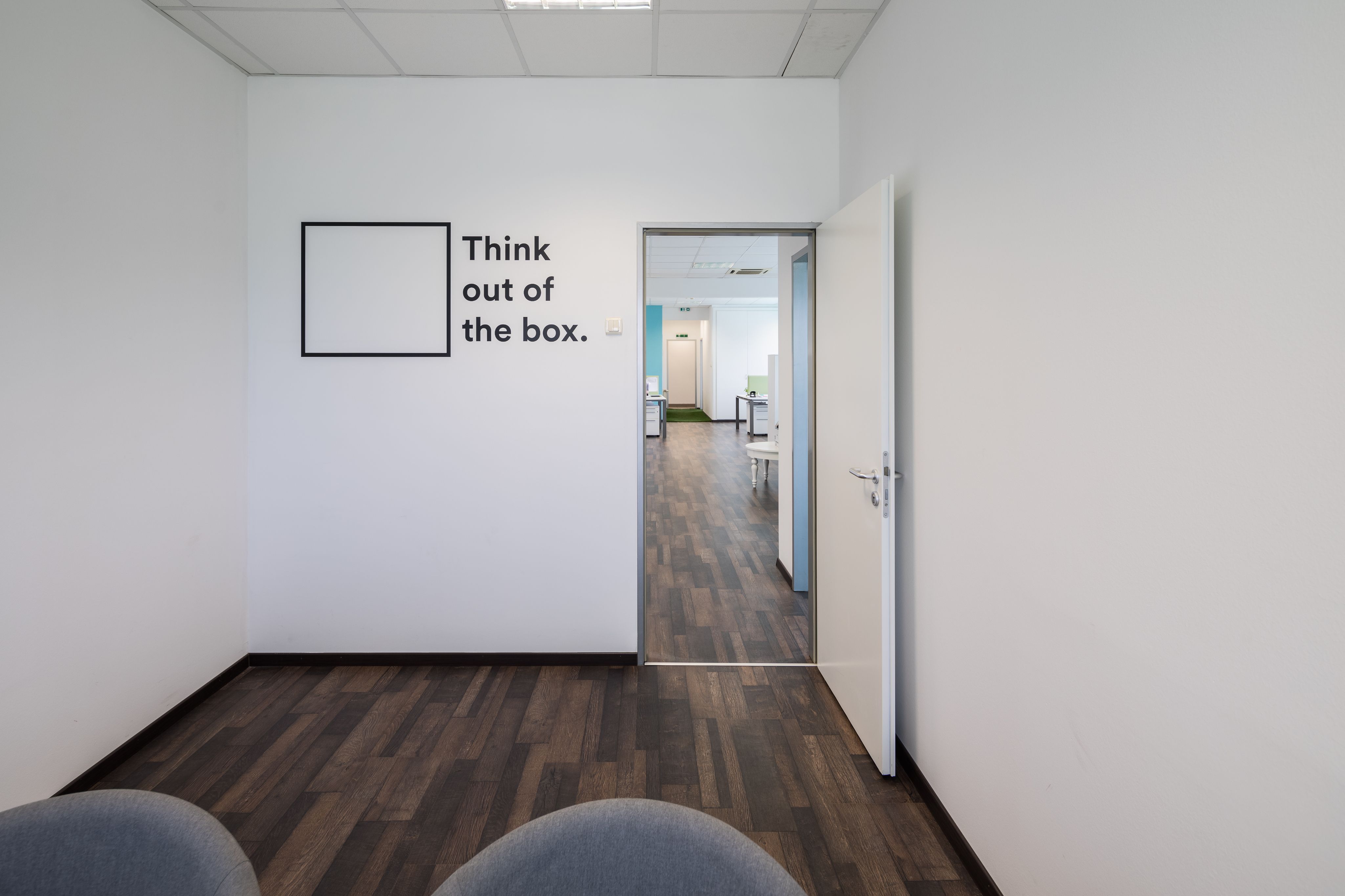 Üres iroda nyitott ajtóval és „Think out of the box.” falfelirattal