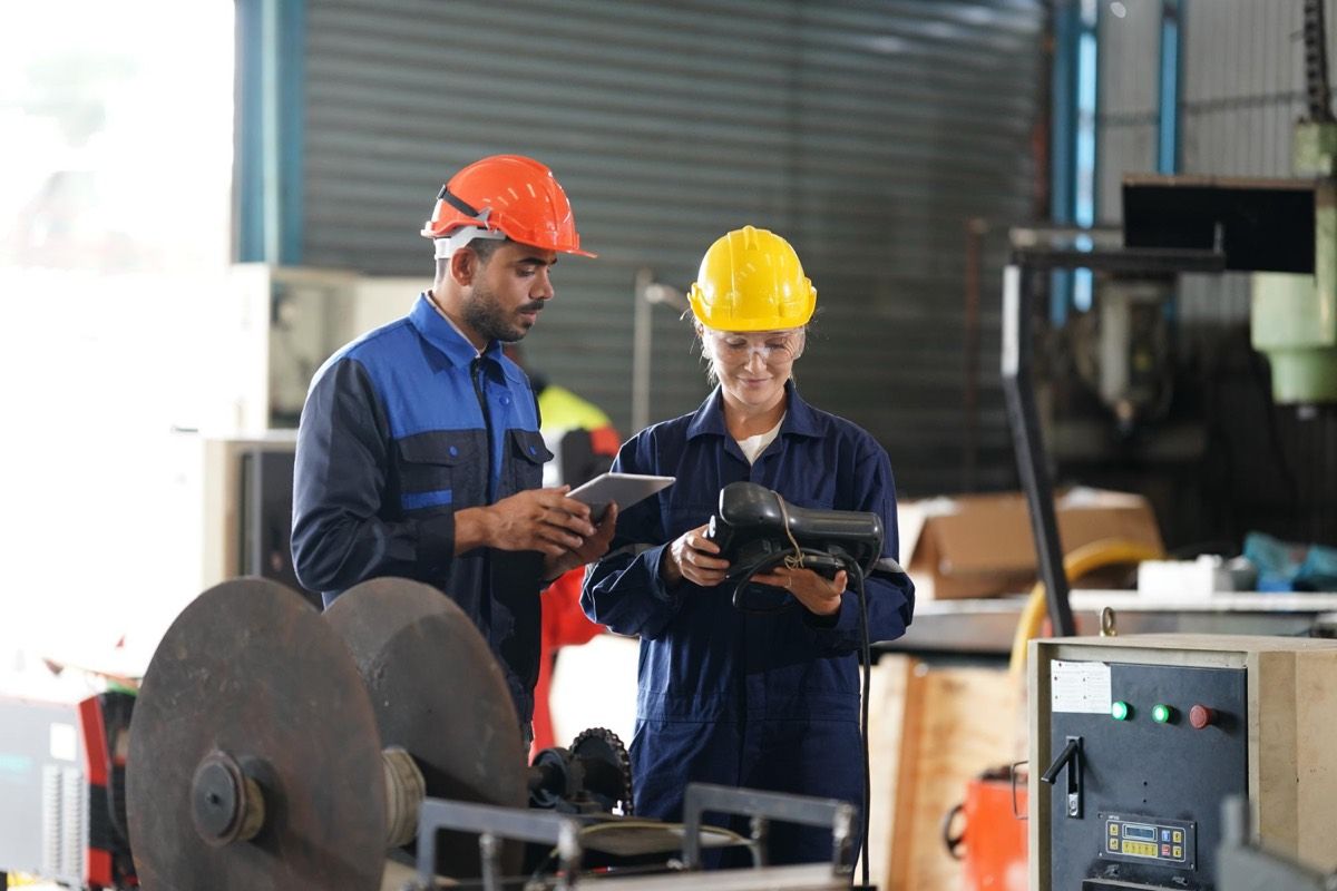 Two workers in hard hats reviewing equipment together on a tablet.
