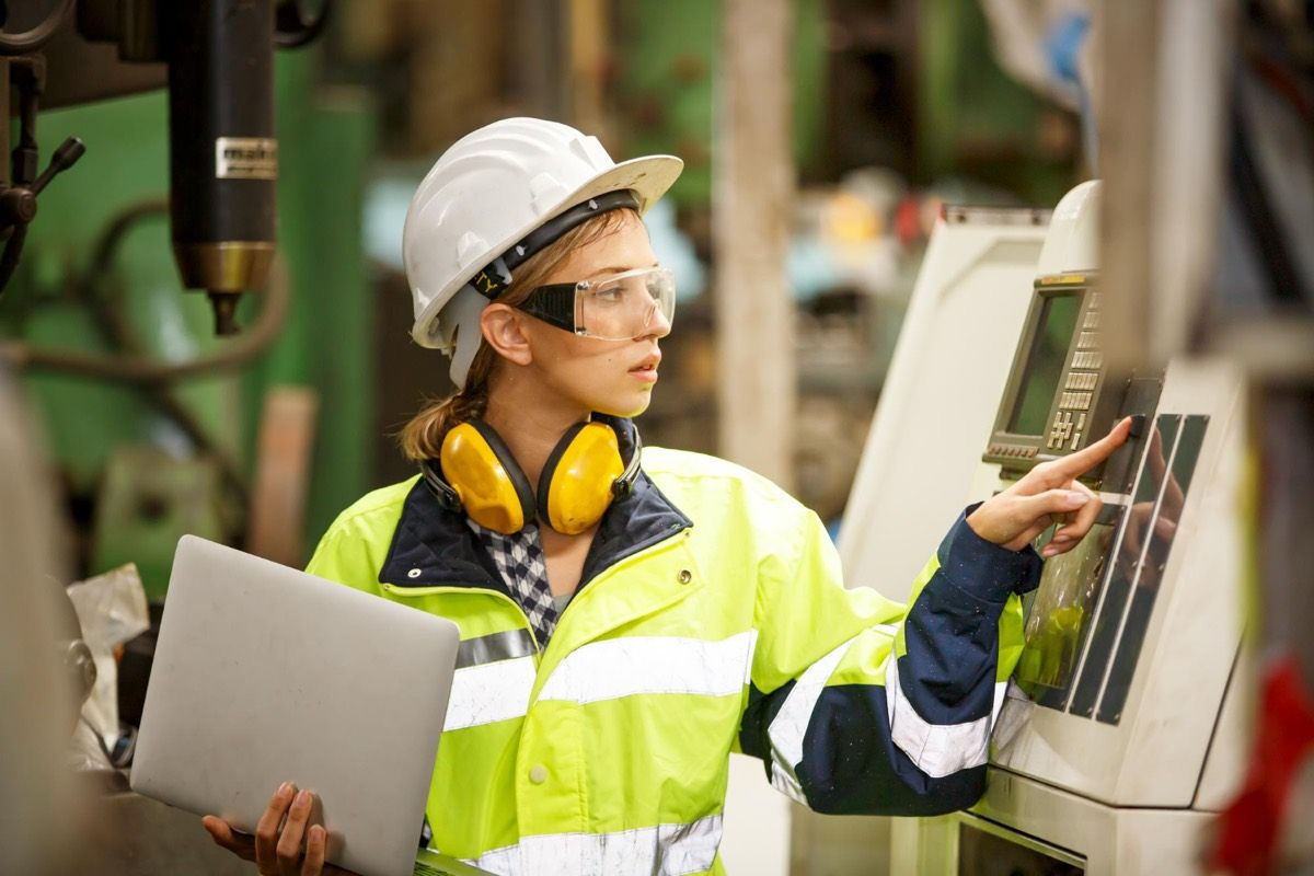 An engineer in protective gear operating a machine control panel.