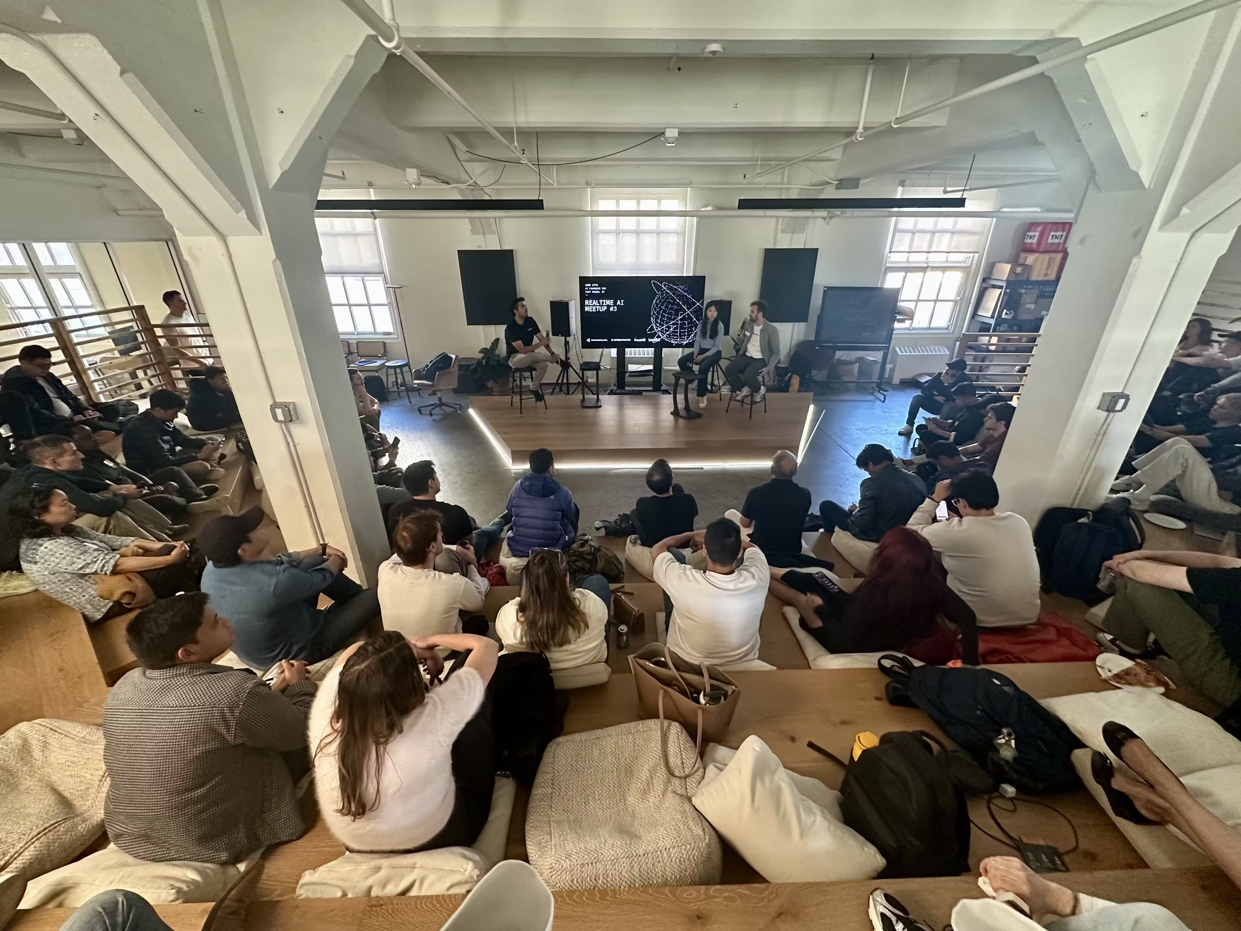 Audience gathered in a modern, well-lit startup office setting to attend a technical presentation or panel discussion.