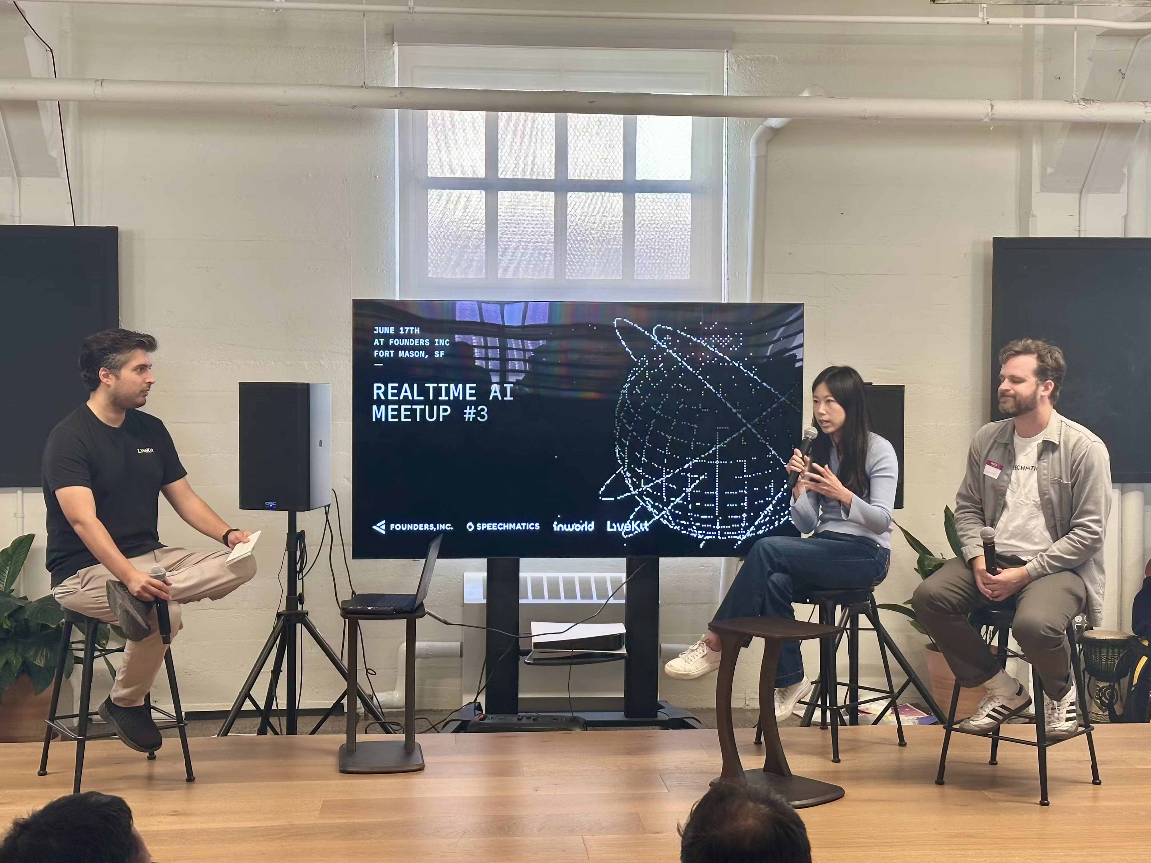 Panel of three people on stage presenting at an event, with the title 'REALTIME AI MEETUP #3' visible on the screen.