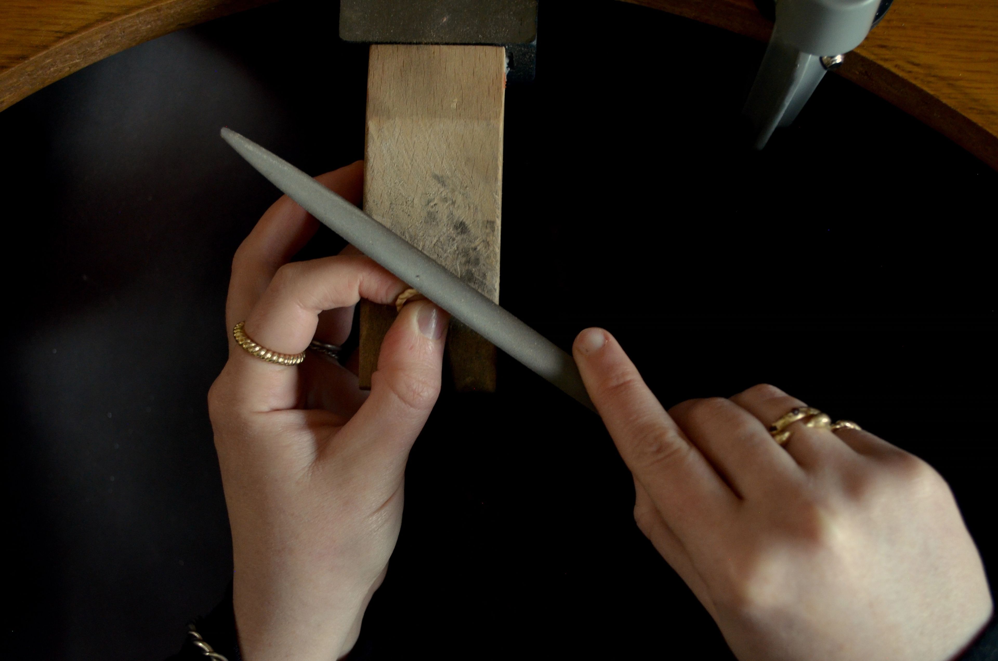 A woman works on a piece of jewellery at a work bench by lamplight