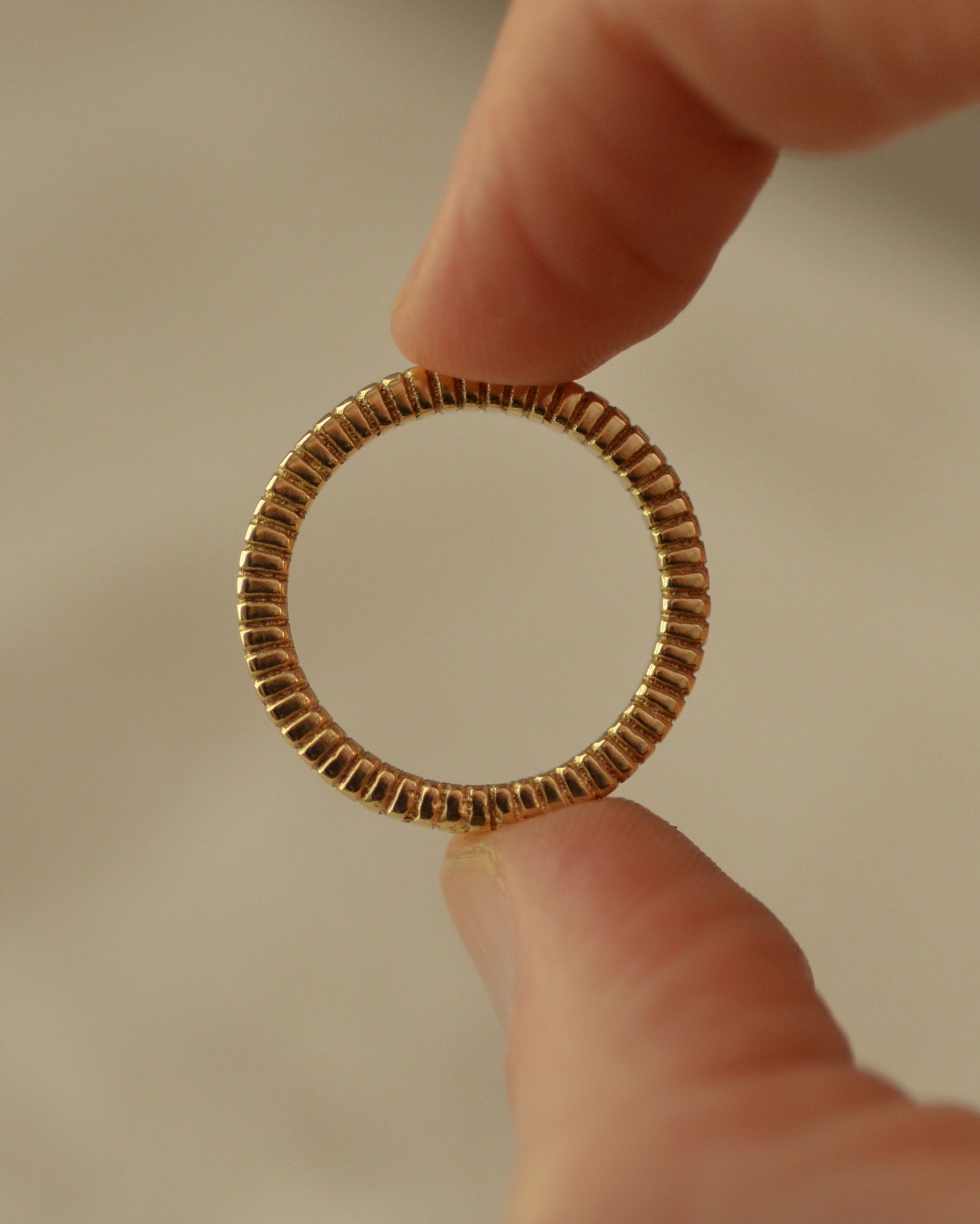 Gold ribbed ring held between fingers