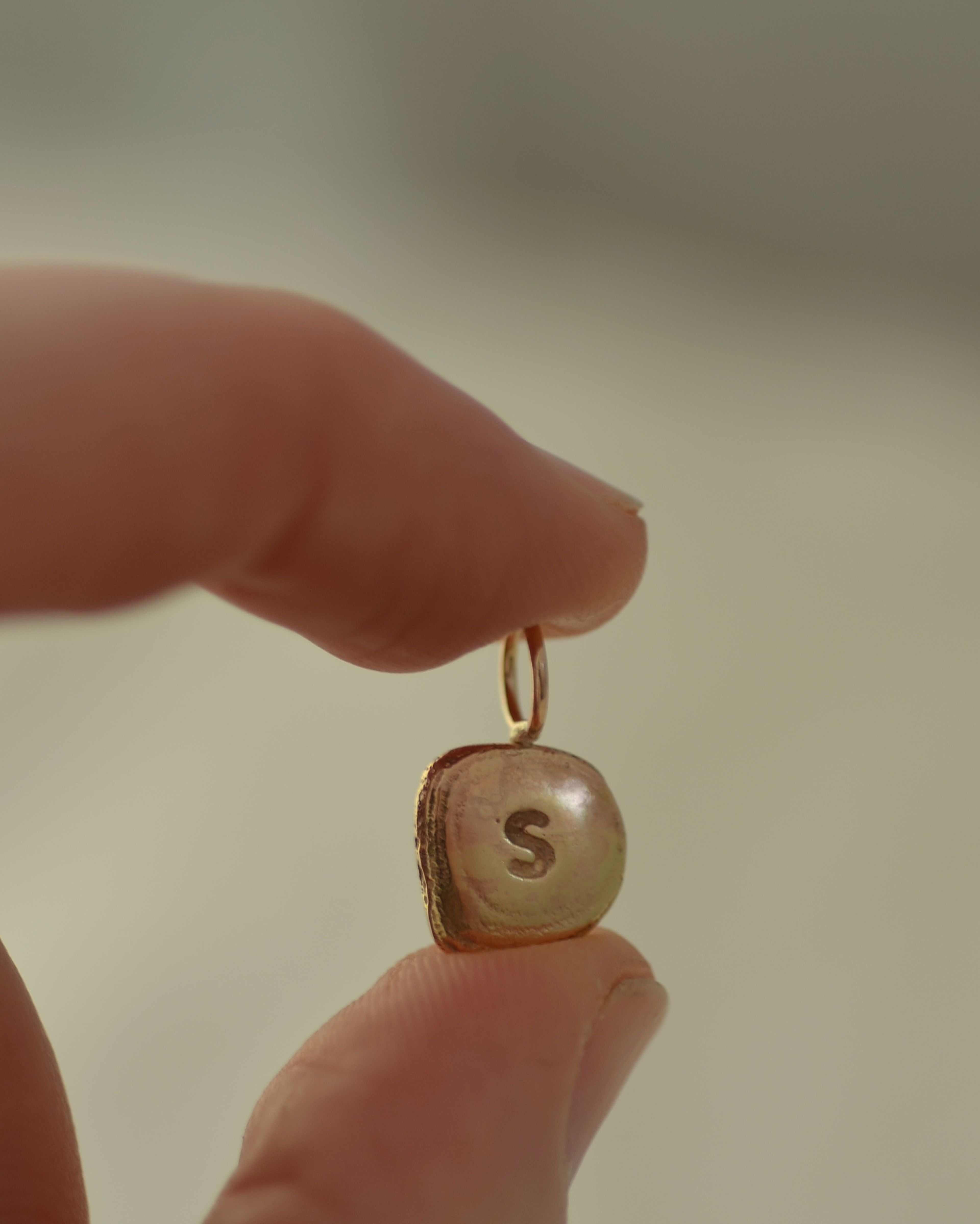 Gold "S" initial pendant held between fingers