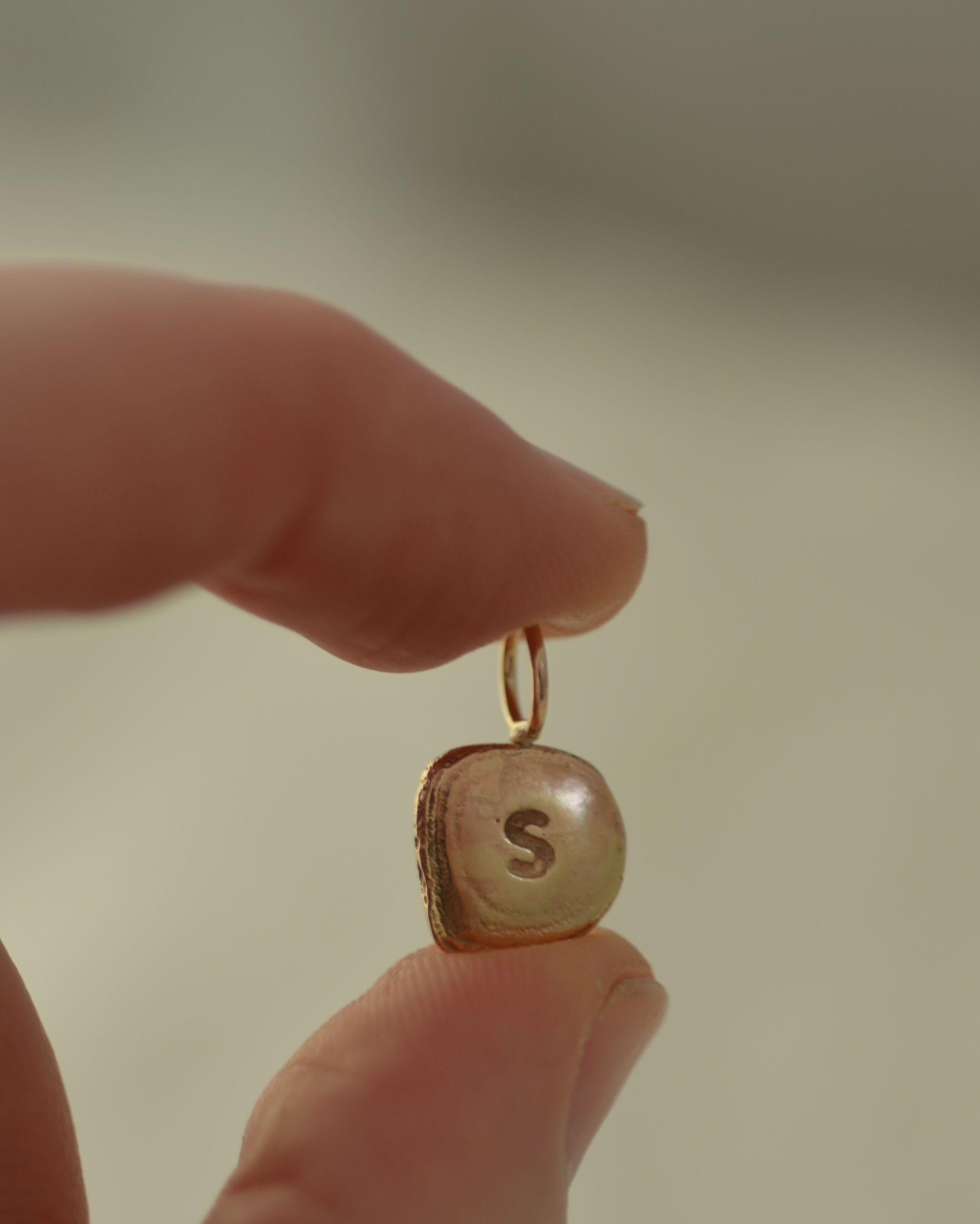 Gold "S" initial pendant held between fingers