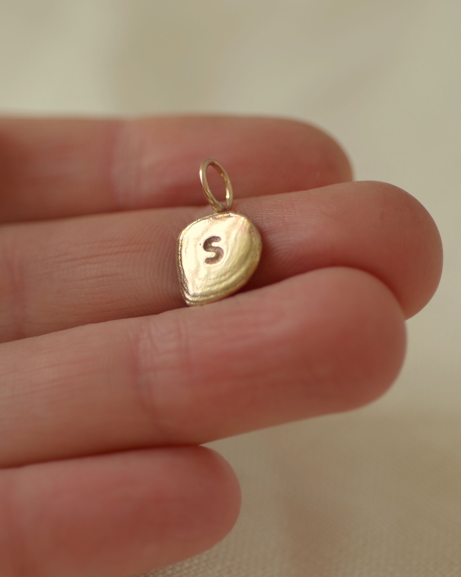 Gold "S" initial pebble pendant held in hand