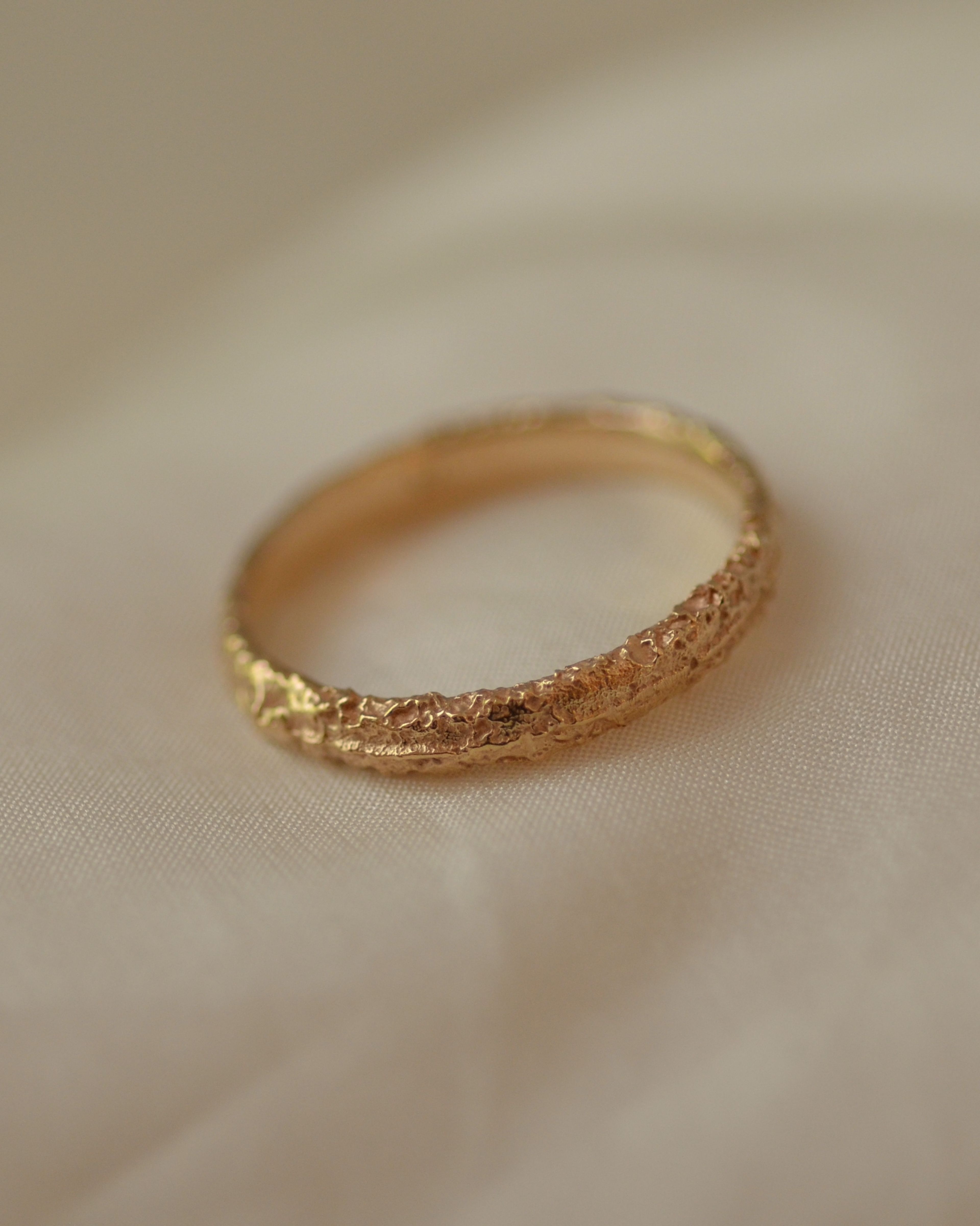 Salt textured solid gold ring on cream silk