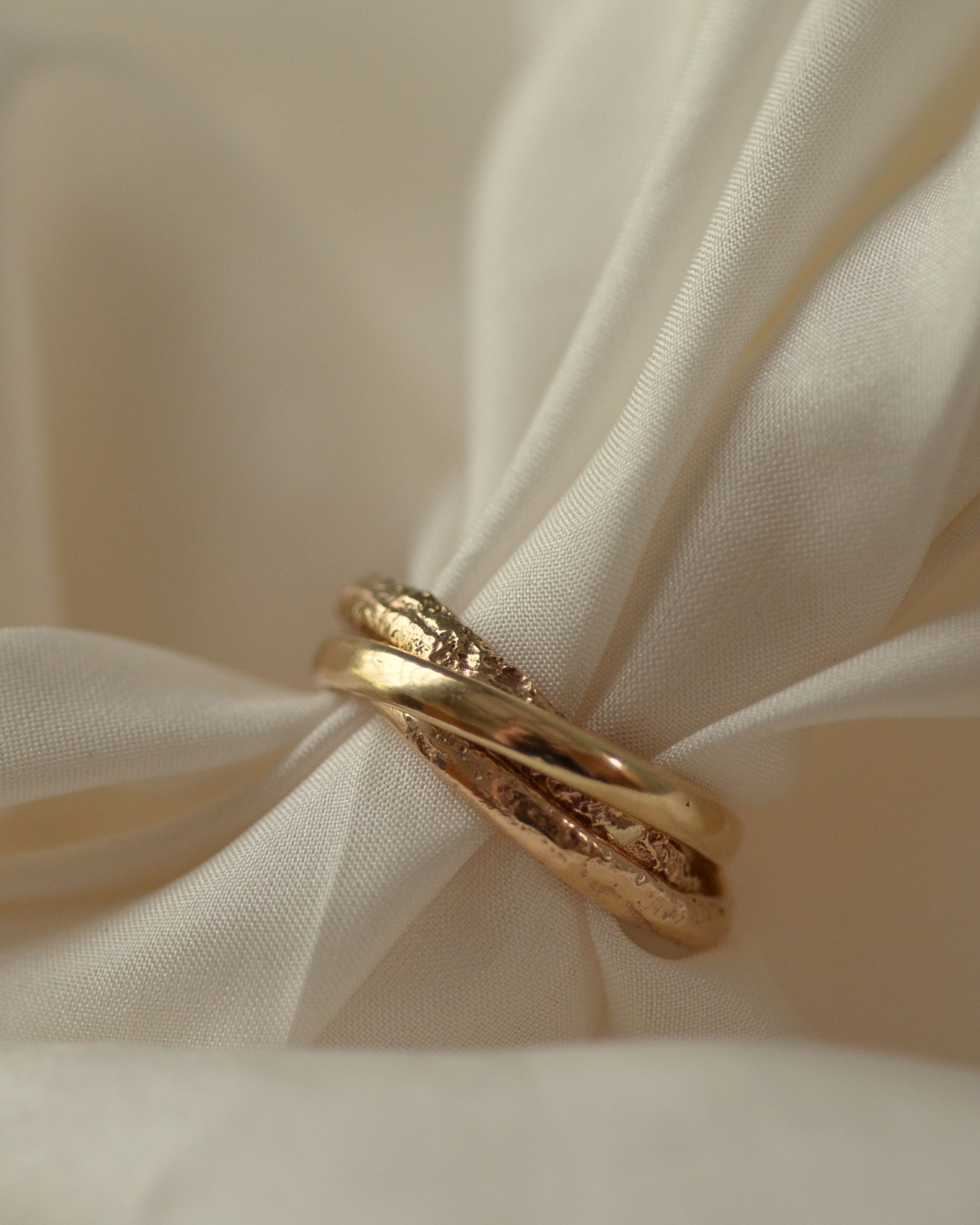 Triple intertwined gold band trinity ring in solid gold with erosion texture on cream silk