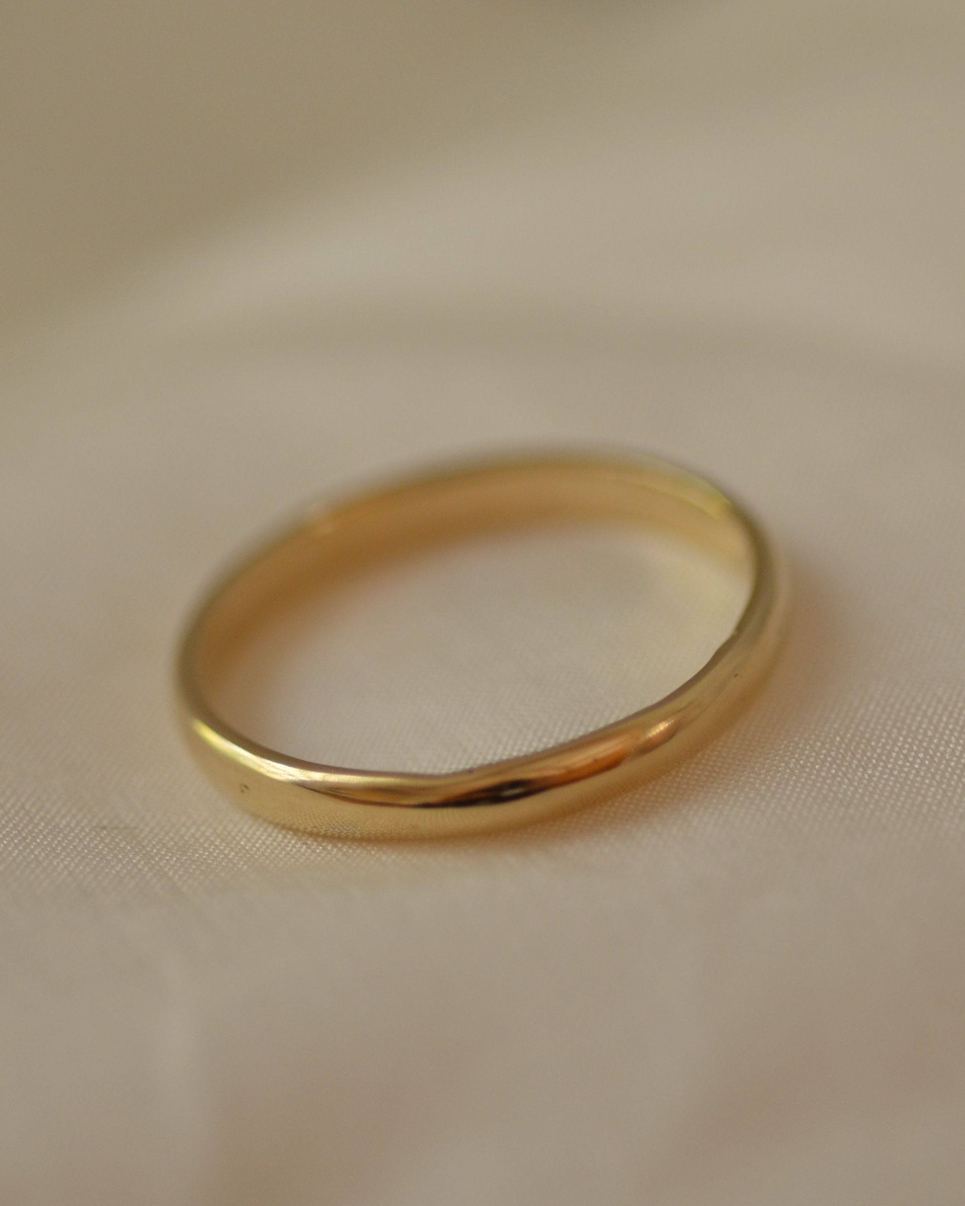 Smooth polished gold band ring on cream silk