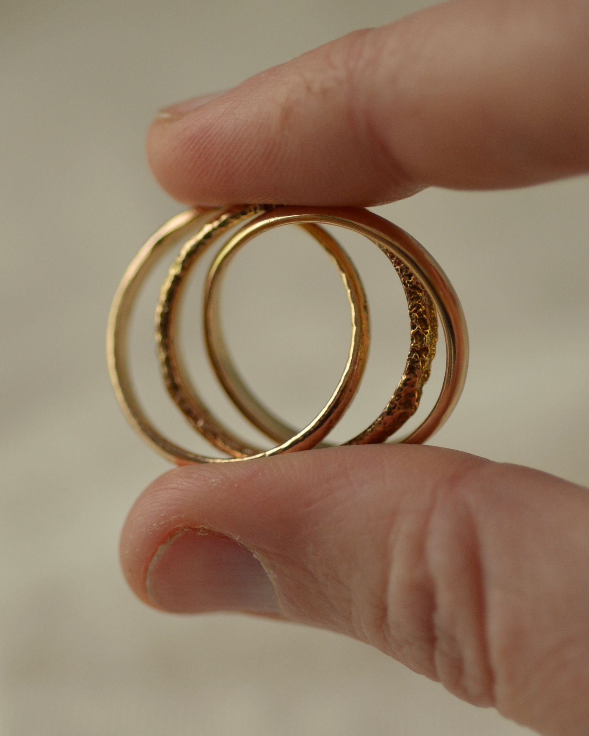 Erosion three intertwined gold rings of different textures held between fingers