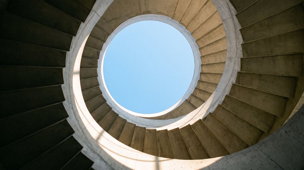Looking straight up a concrete spiral stairwell to a circle of sky