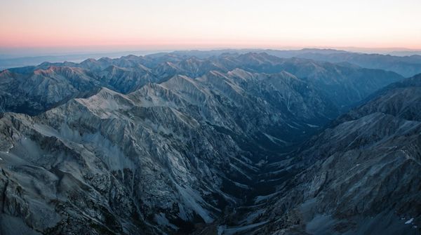 An aerial view of long ridgelines receding to a pale dawn horizon