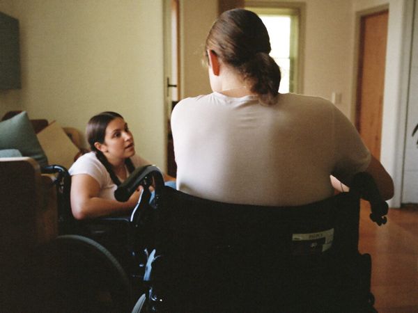 Two people talking at home, one using a wheelchair, seen from behind
