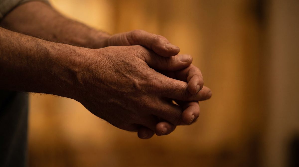 Two hands lightly clasped, close, against a soft warm background