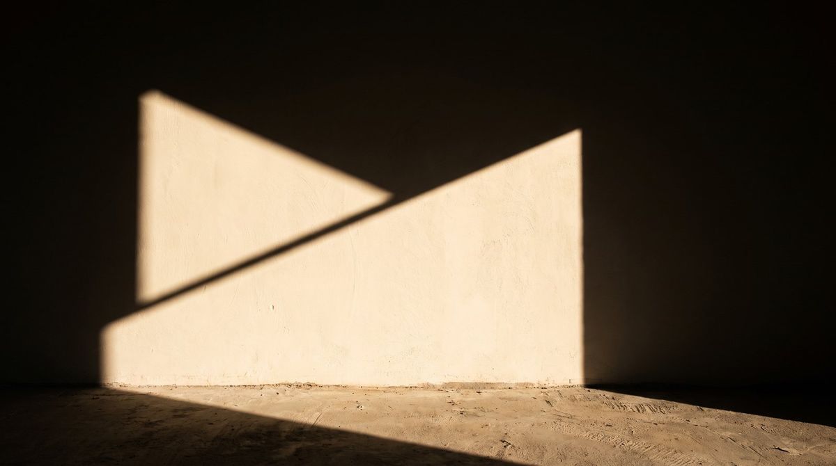 A hard diagonal band of afternoon sun cutting across a plain cream wall