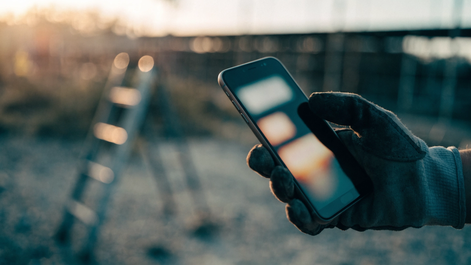 A work-gloved hand holding a smartphone at a job site at dawn, an abstract layout glowing on the screen