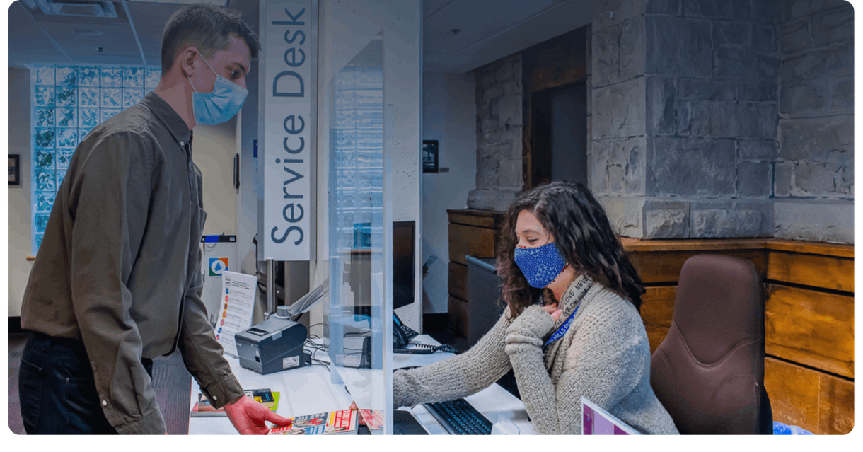 A visitor at the library service desk with a staff member