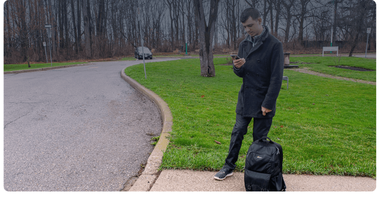 A rider with a backpack checks a phone at the curb