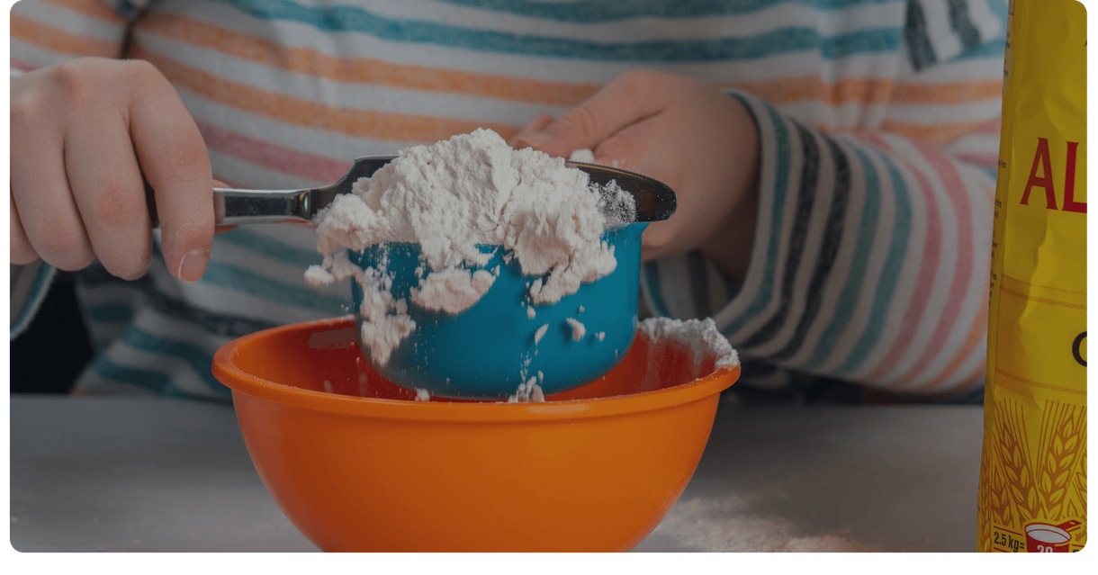 A baker scoops flour into a mixing bowl
