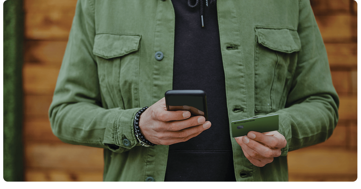 A customer holds a phone and a green debit card